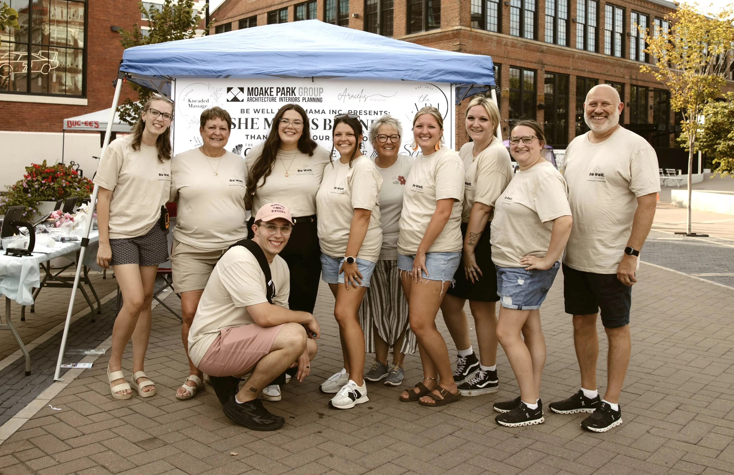 a group of adults both female and male standing together for a group picture in front of a She Means Business sign at an event
