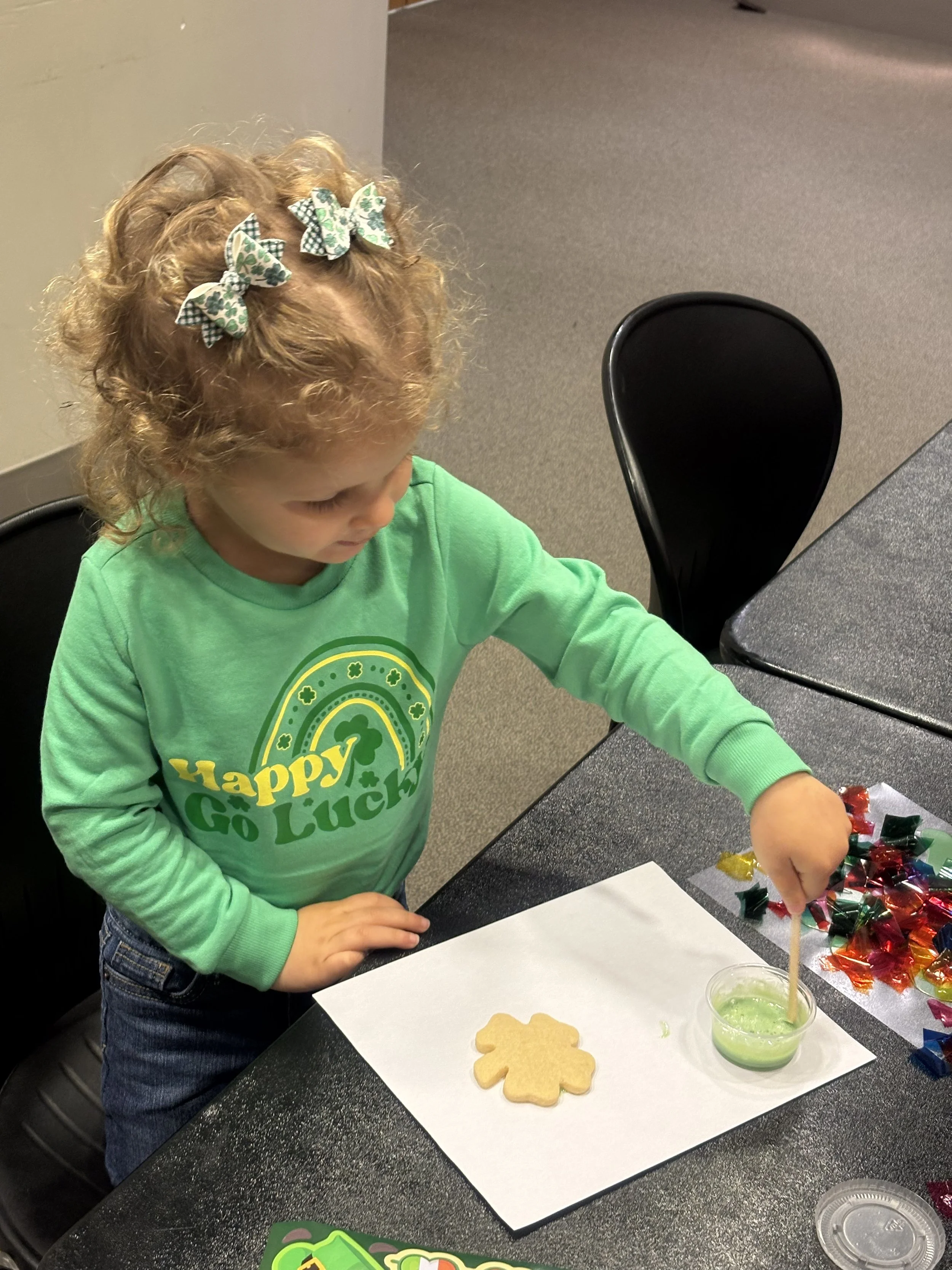 a toddler wearing all green decorates a shamrock cookie for St. Patricks Day