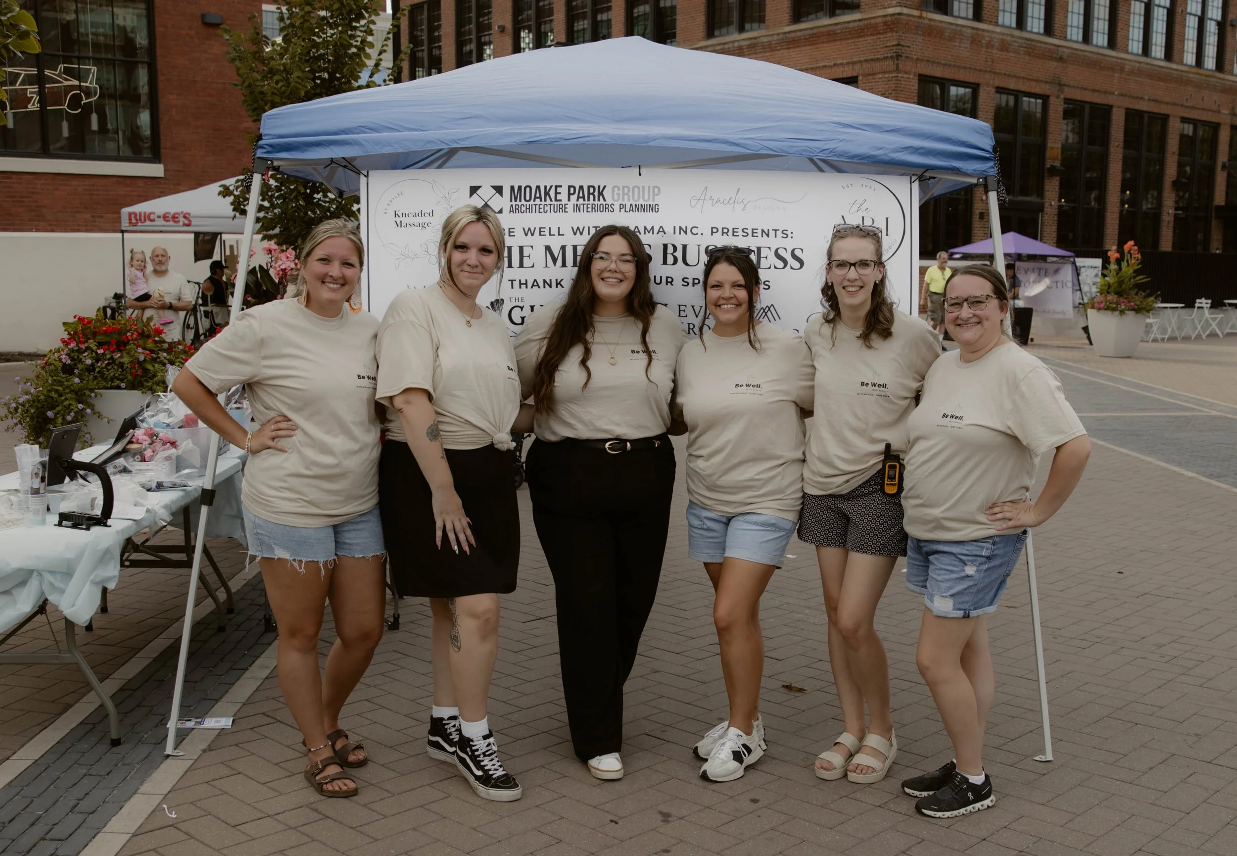 the be well with mama board at She Means Business in 2025. It is a city landscape with vendor tents in the background