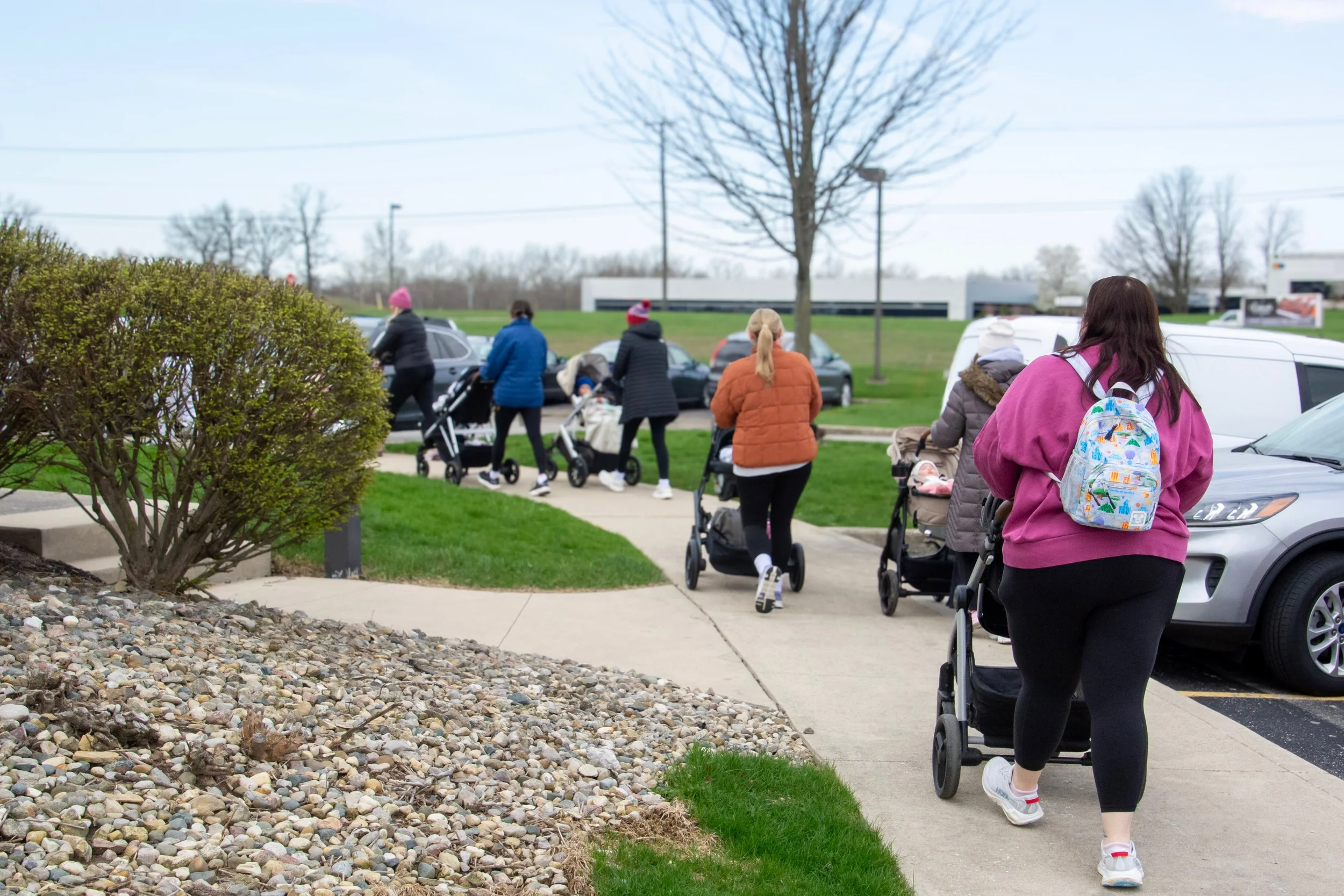 a collection of moms walking away from the camera with their children in strollers.