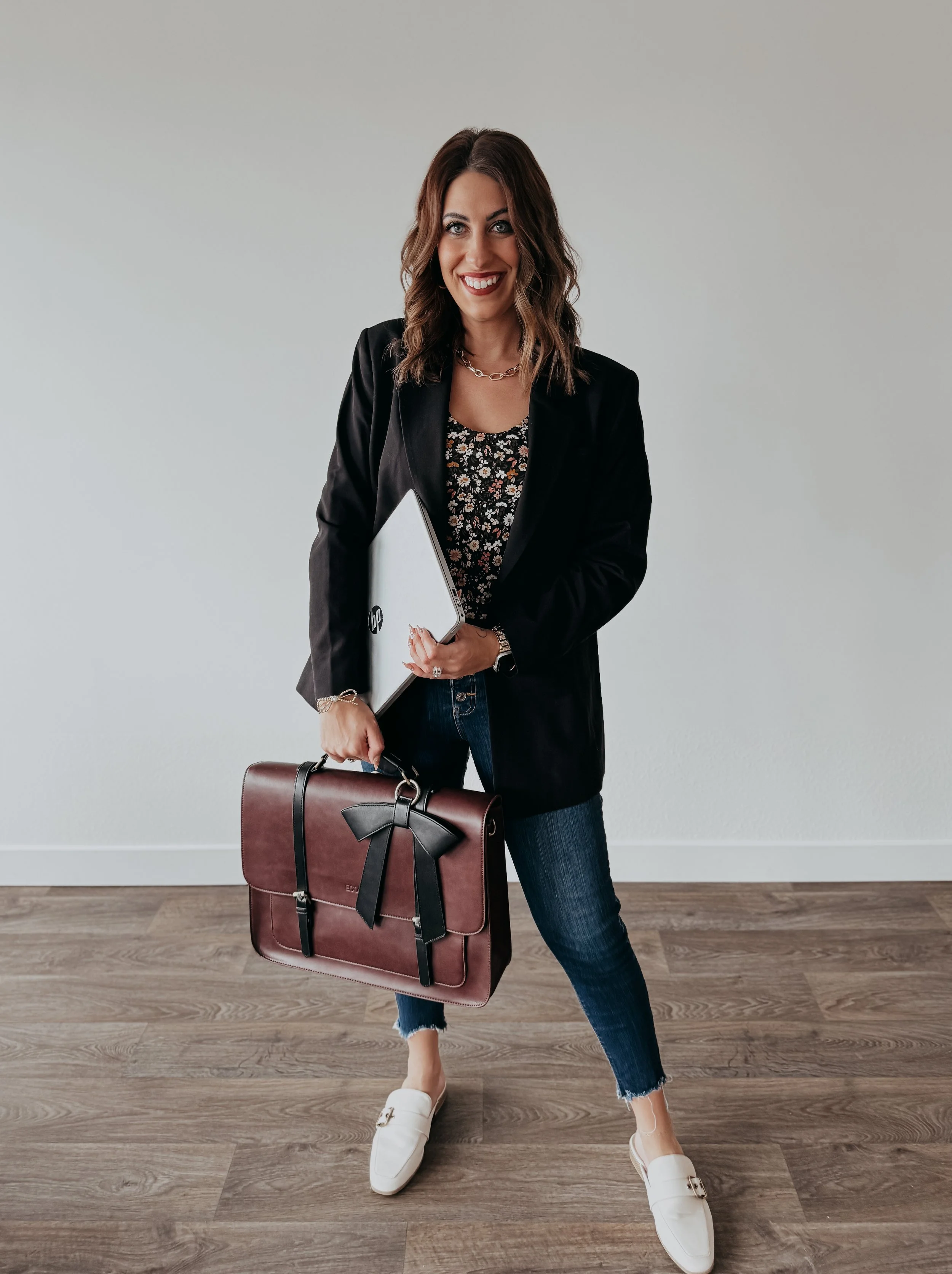 a woman with dark brown hair smiling and holding her briefcase and laptop