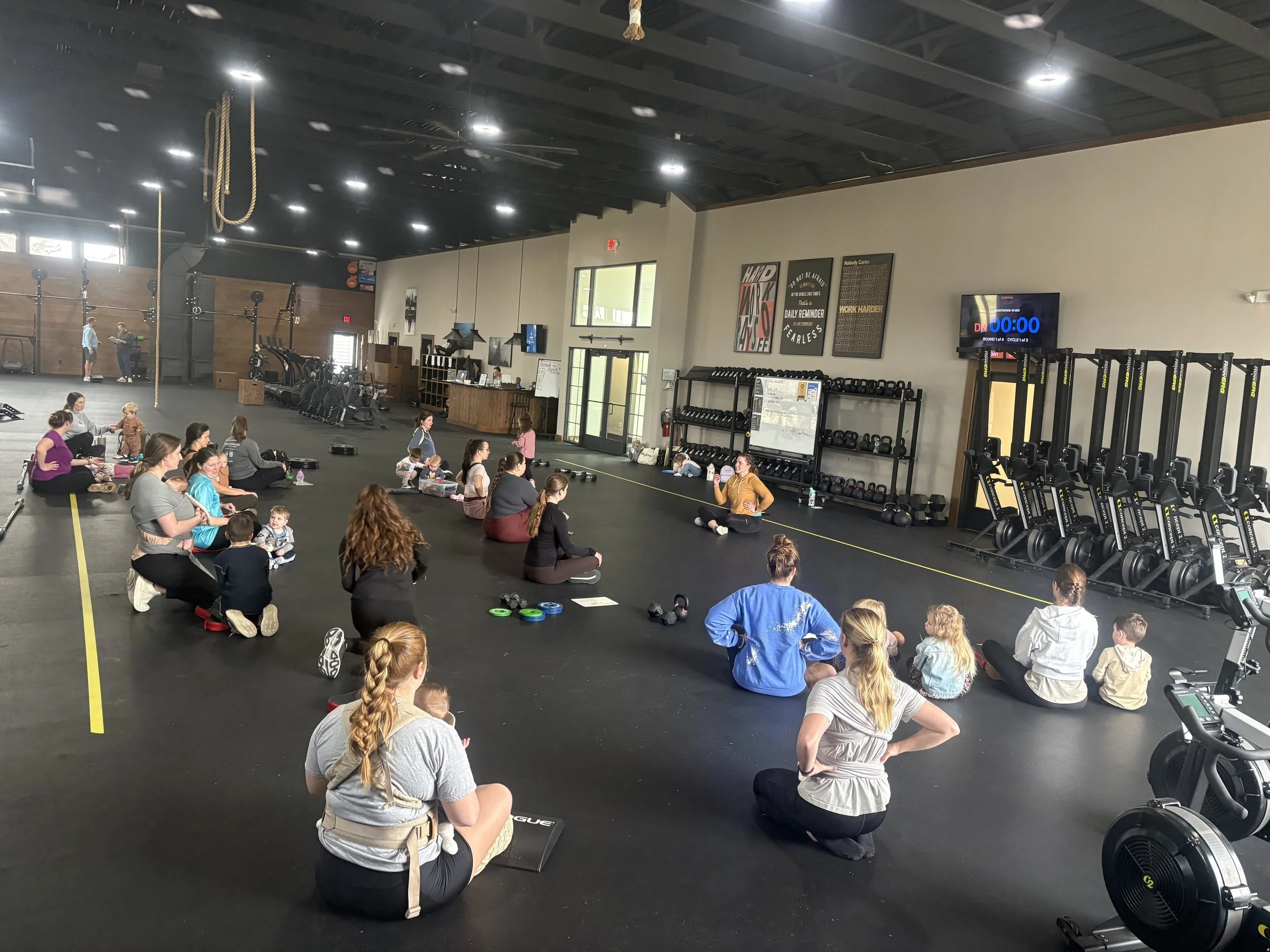 around 20 moms some with their young children others are baby wearing sitting and stretching at an exercise class