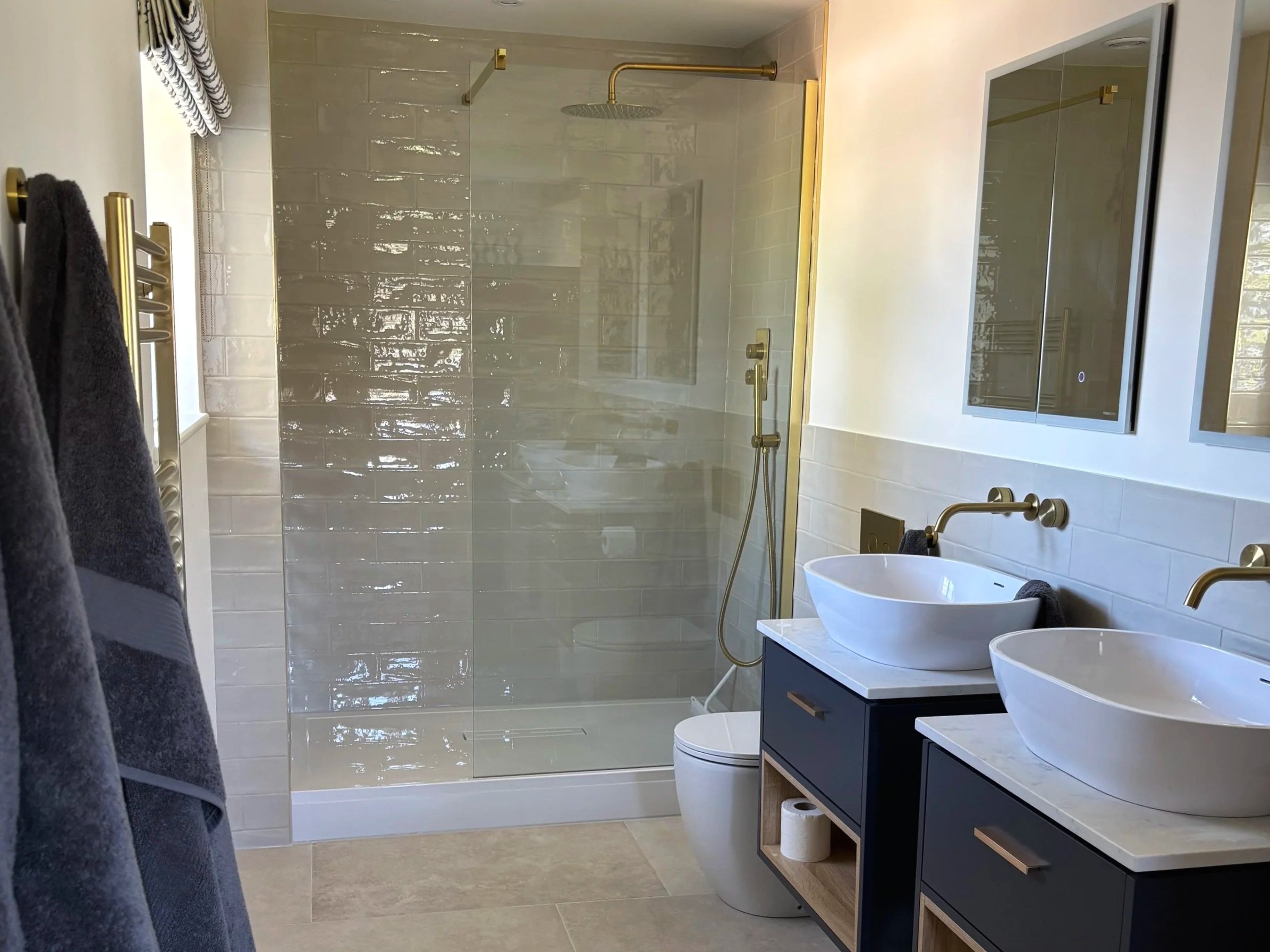 Modern bathroom with a shower stall featuring glass doors, a rainfall showerhead, a white bidet, a black vanities with two vessel sinks, a large mirror, and dark towels hanging on a heated towel rail.