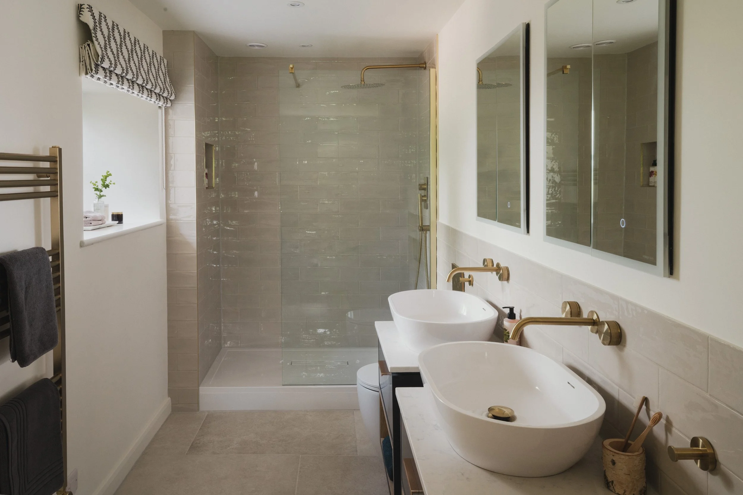 Modern bathroom with dual vessel sinks, large mirror, and shower area with gold fixtures and glass enclosure.