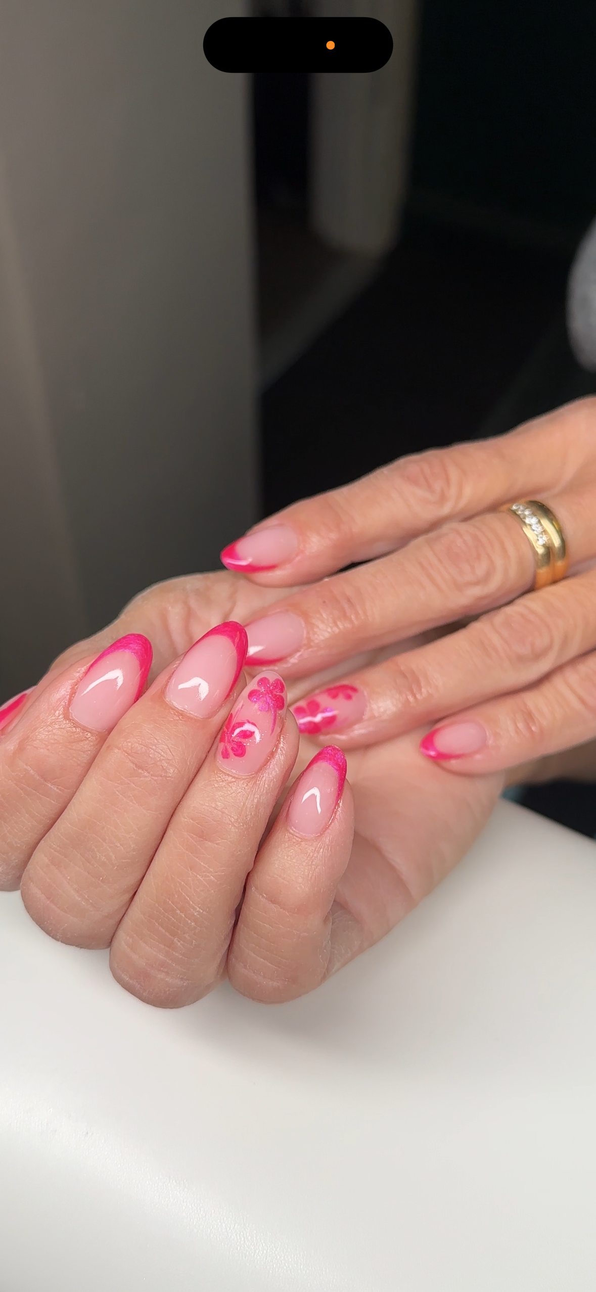 Nära bild av en hand med nylagda naglar som har rosa och vita blomsterdesigns samt rosa kanter.