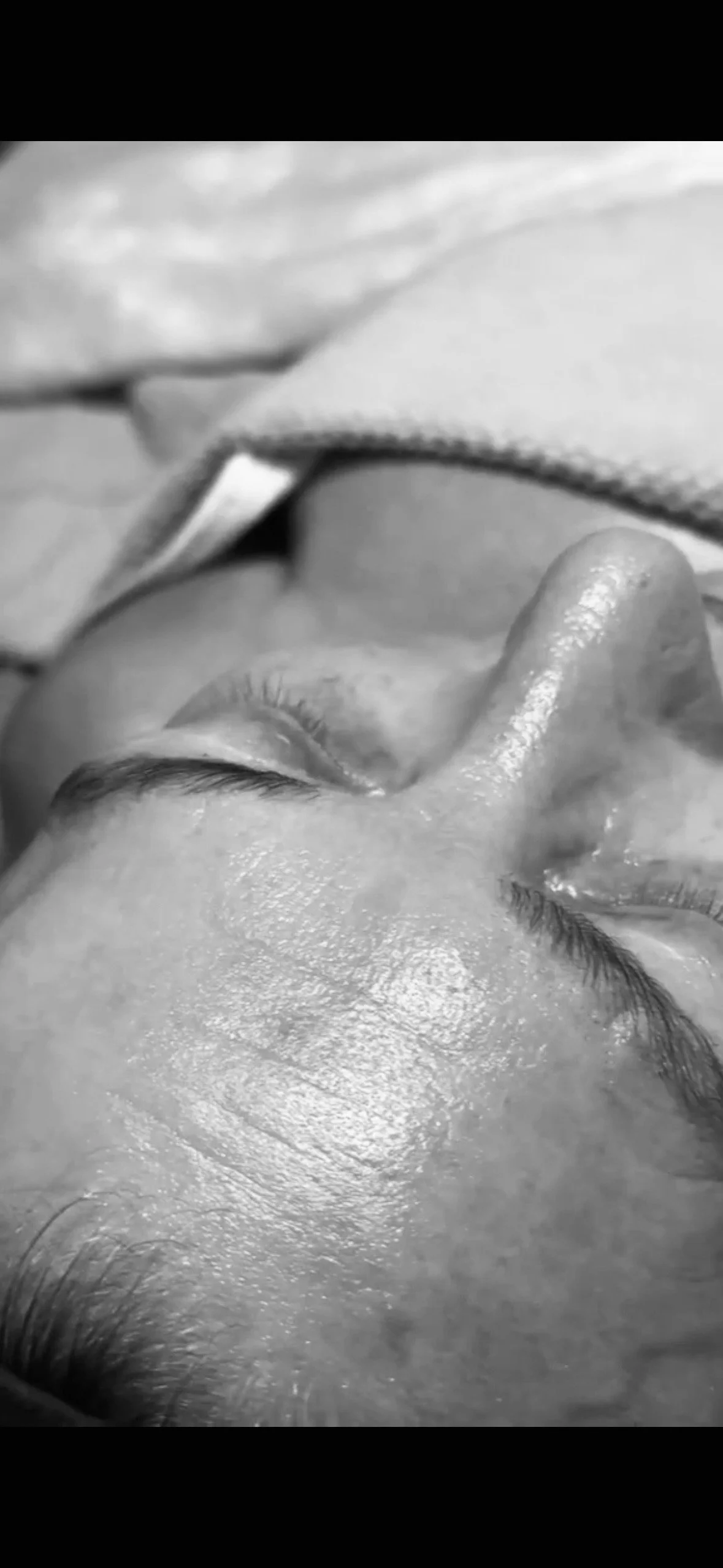 Svartvitt foto av en person som sover med ögonen stängda, liggande på sidan. Personen har släta ansiktsdrag och lång ögonfransar.