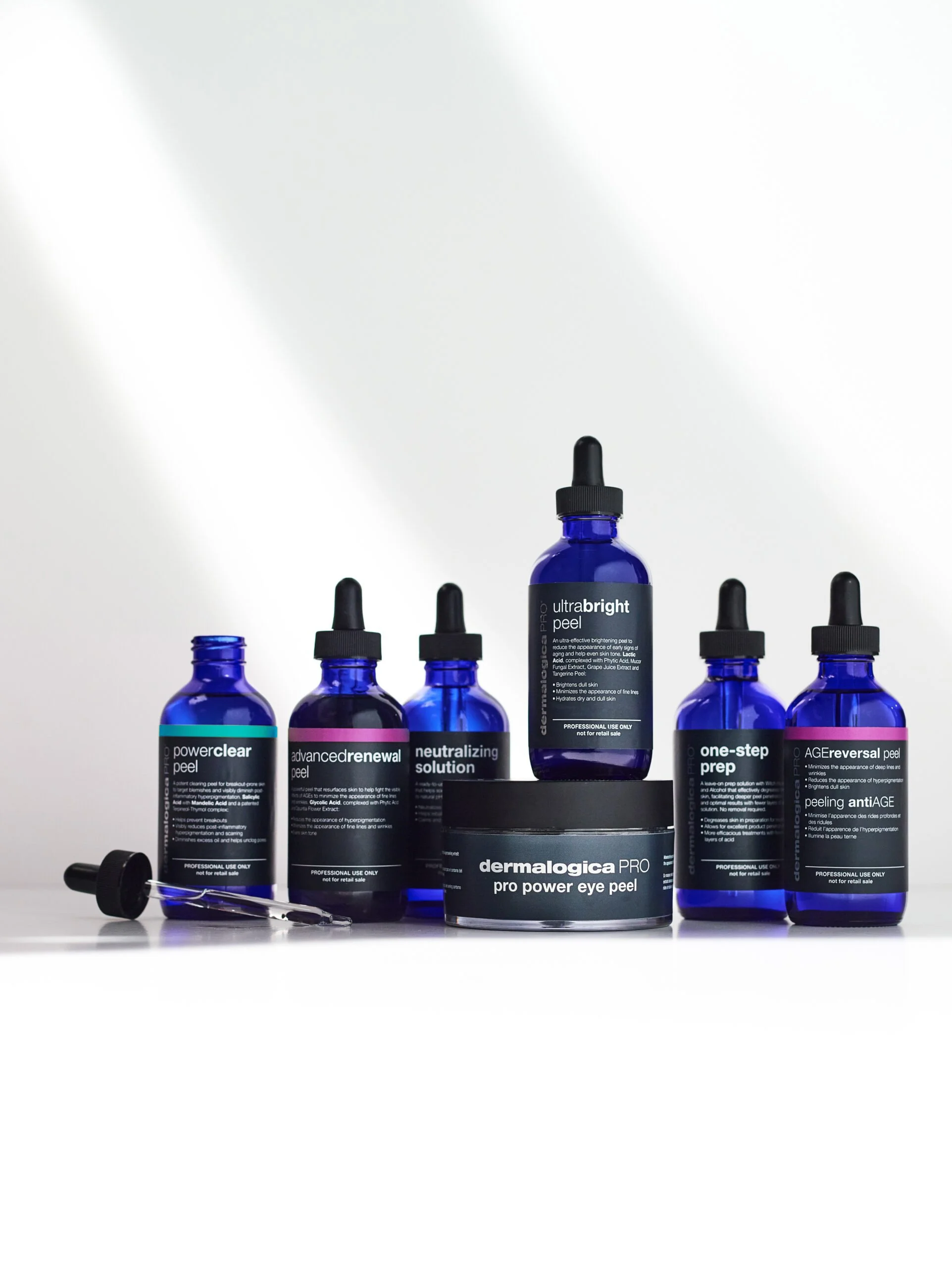 Sex blå flaskor med olika hudvårdsprodukter, inklusive peelingen dermalogica PRO pro power eye peel i mitten, på en vit bakgrund.