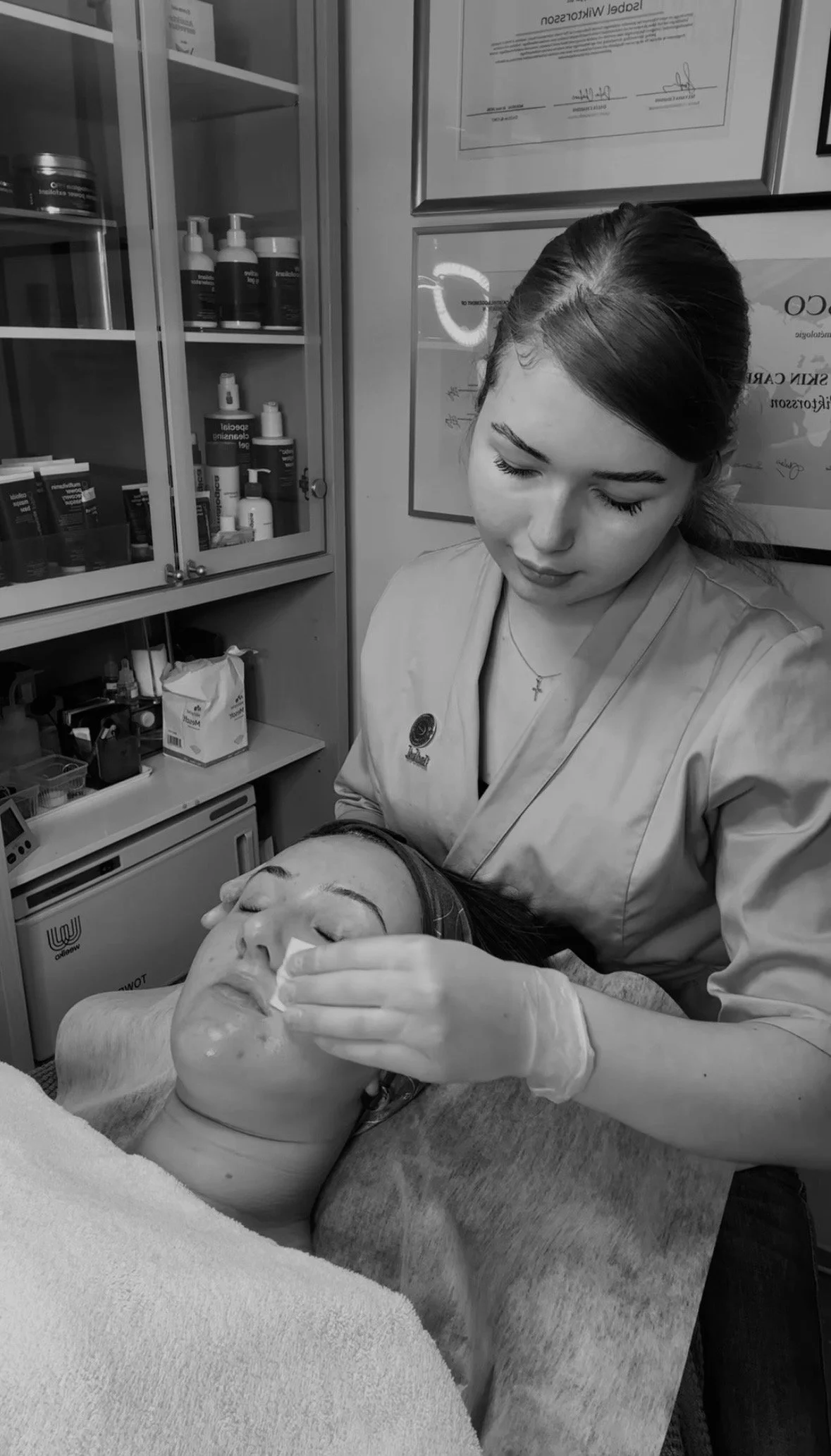 En sjuksköterska sköter en patient som ligger på en sjukhussäng. Dåret i patientens ansikte är bandagerat och sjuksköterskan använder en kompress or applicerande behandling. Rummet har medicinska förvaringsskåp på väggarna.