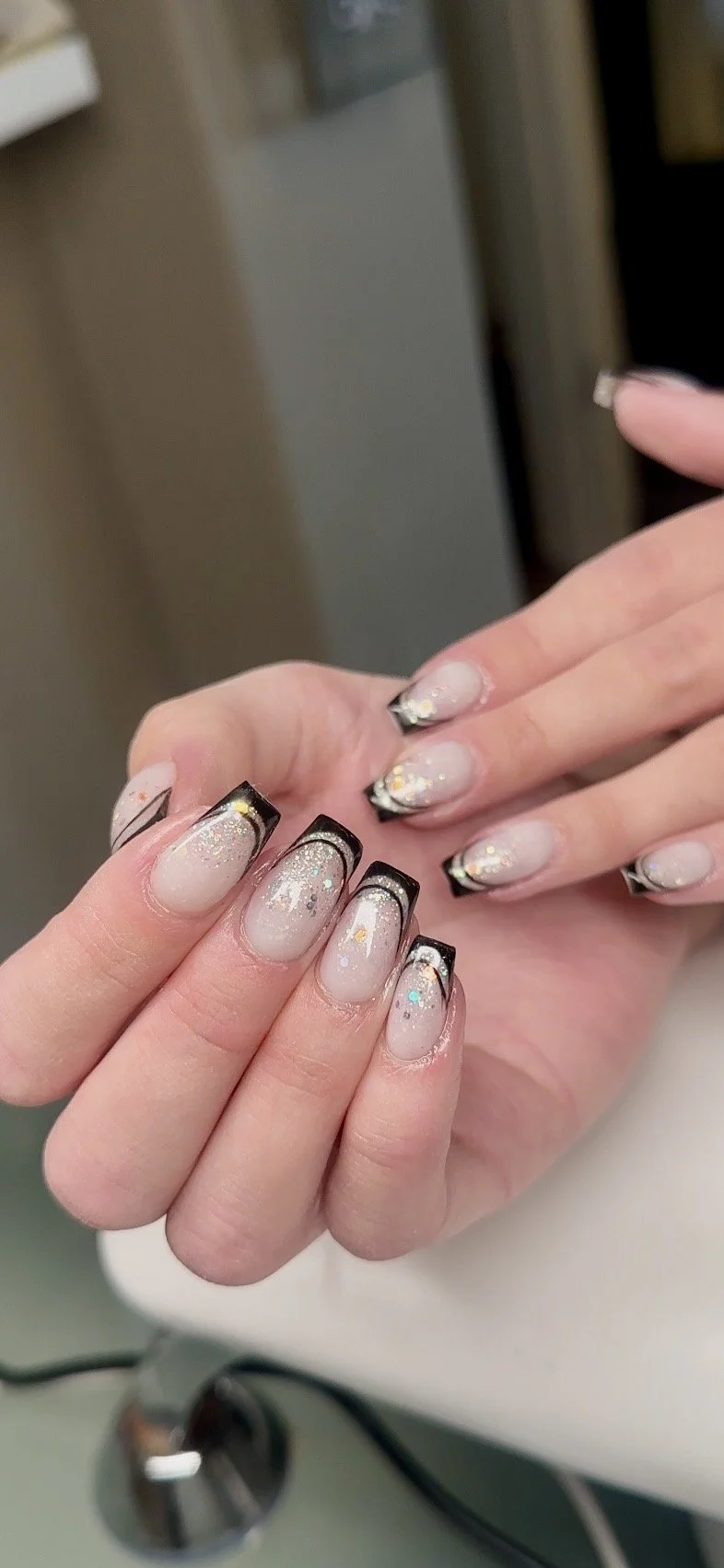 Nagellackade naglar med svartkant, glitter och uringlat mönster på en hand.