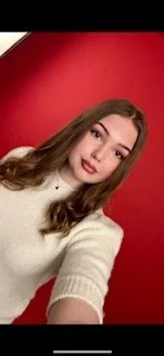 Ung kvinna med långt hår som tar en selfie framför en röd bakgrund.