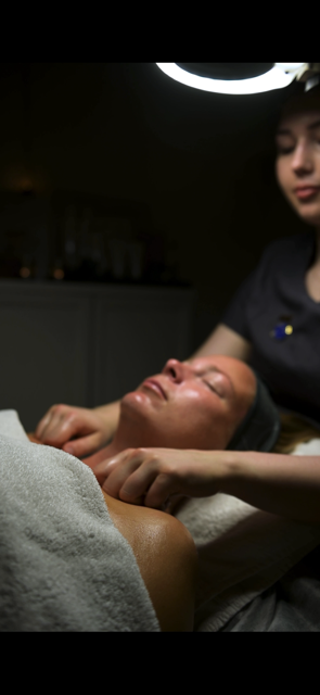 Person som får en ansiktsmassage eller behandling på en klinik, med en hudterapeut eller beautyspecialist som arbetar.