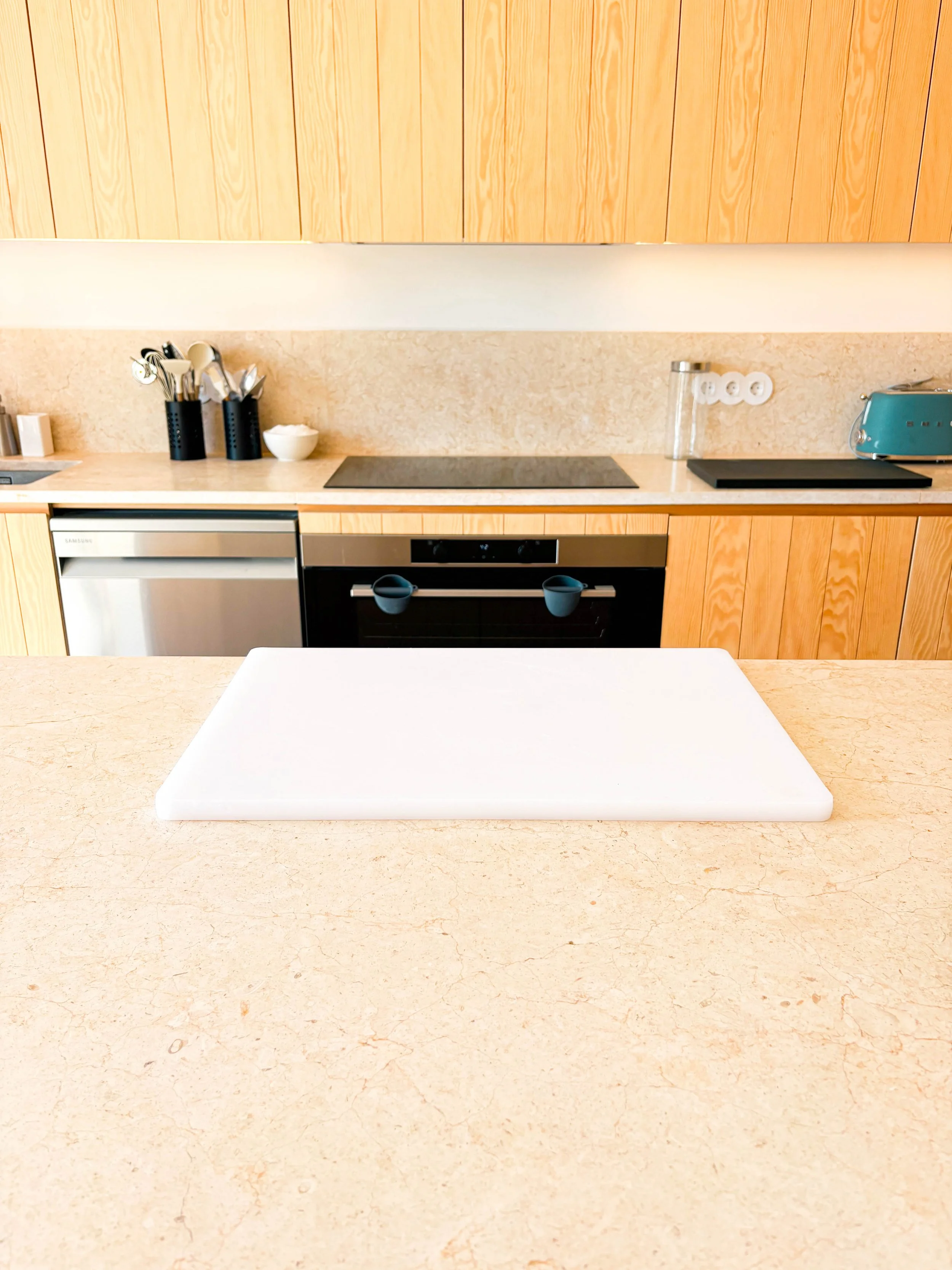 Cozinha moderna com bancada de granito, utensílios de cozinha em porta-copos na geladeira, forno embutido, cooktop, banho-maria e uma torradeira azul. Número de tomadas, recipiente de vidro e utensílios em suportes pretos.