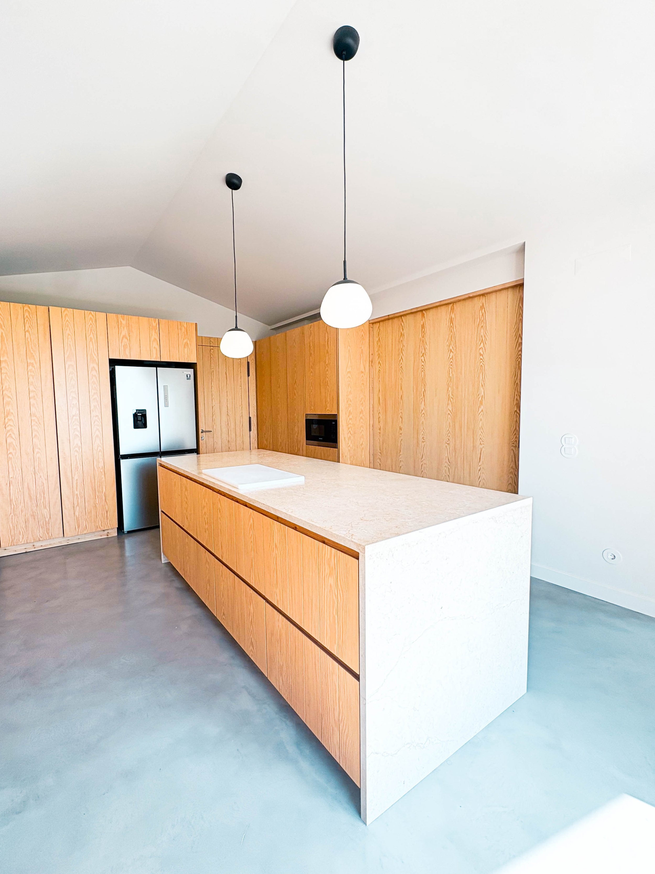 Cozinha moderna com ilha de mármore clara, armários de madeira e iluminação pendente