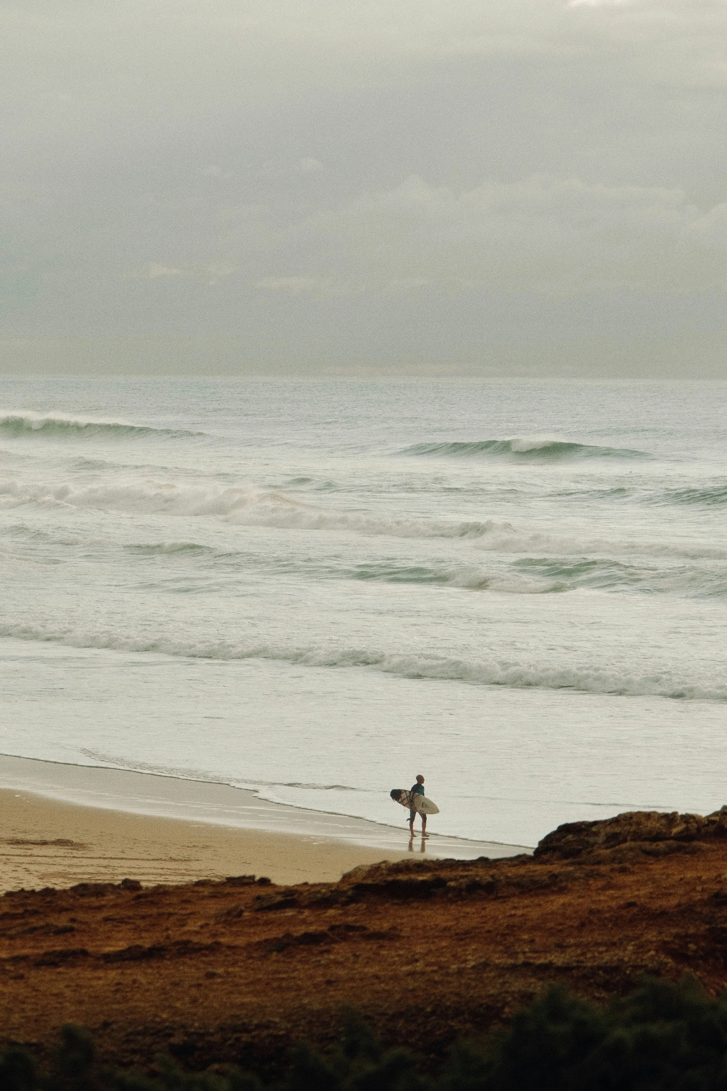 Pessoa com prancha de surfe caminhando na praia ao pôr do sol