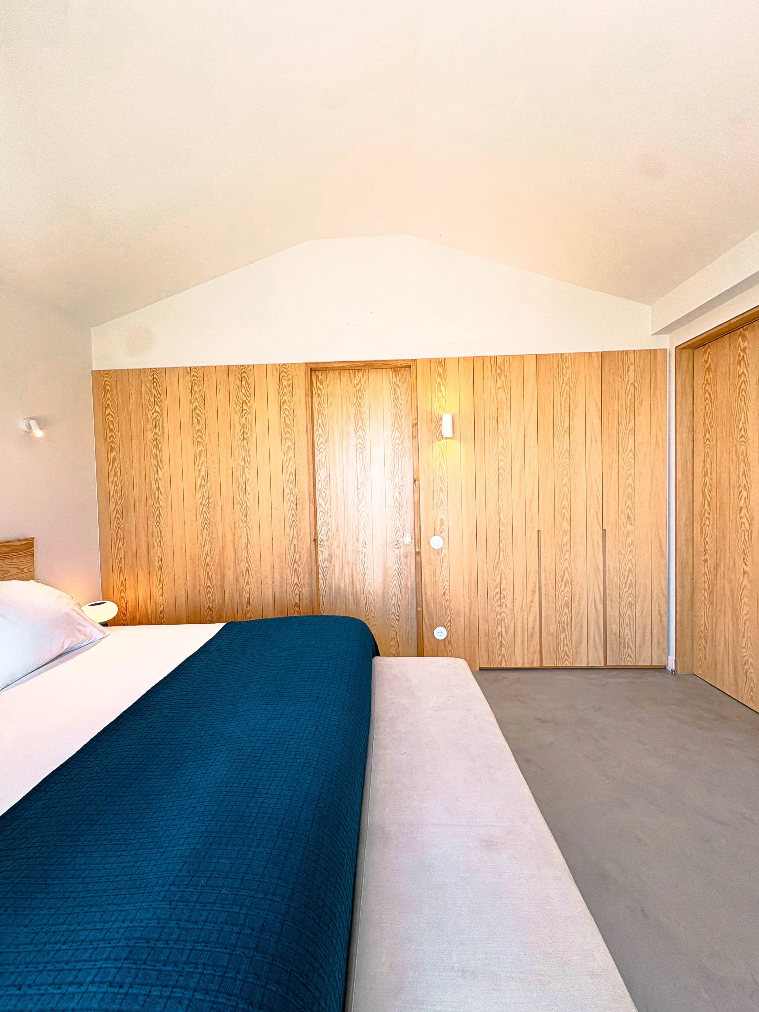 Quarto com cama, cabeceira de madeira, parede de madeira do chão ao teto e iluminação amarelada.