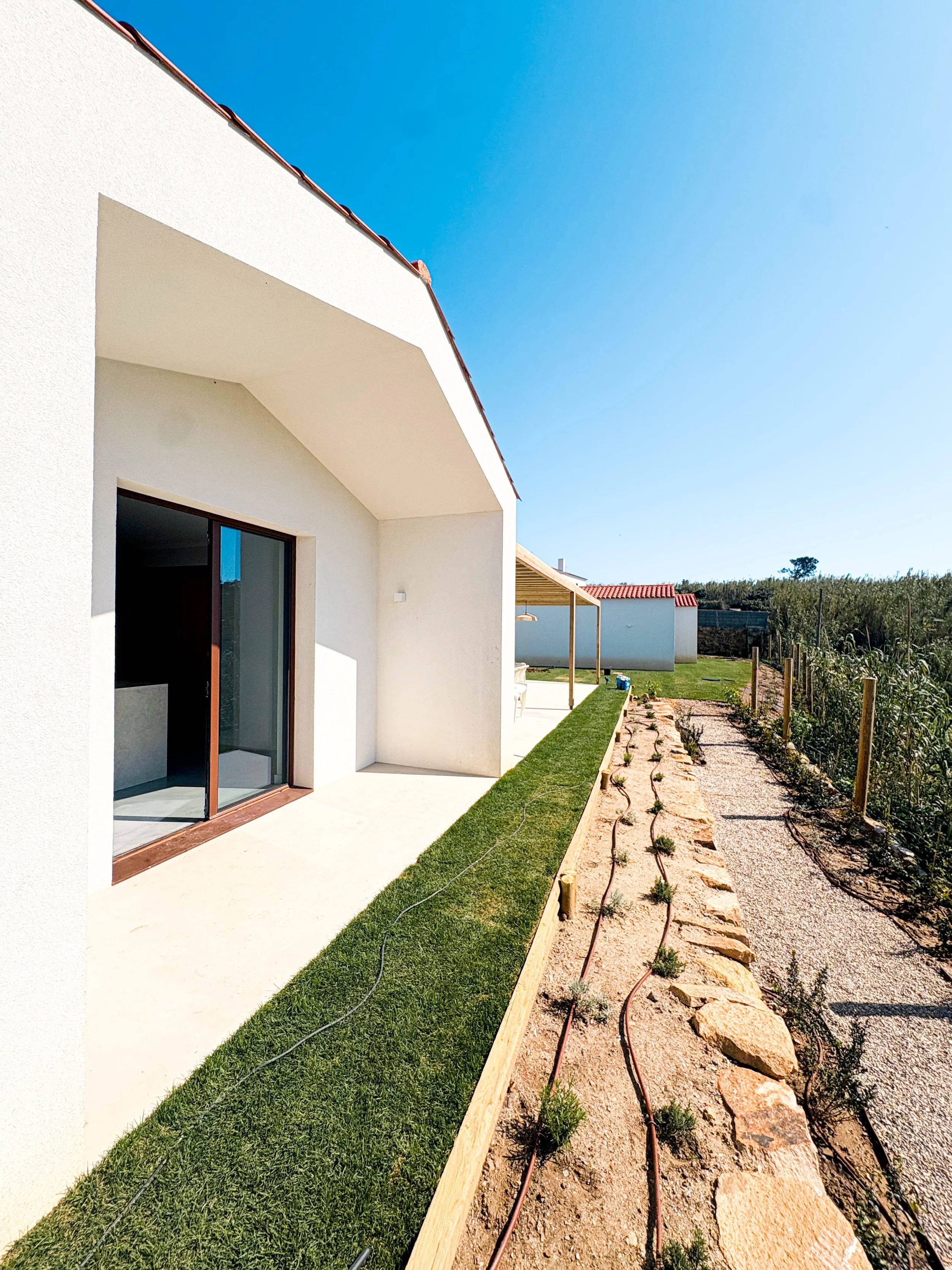 Casa moderna com espaço externo, jardim recém-plantado, caminho de pedras e sistema de irrigação.
