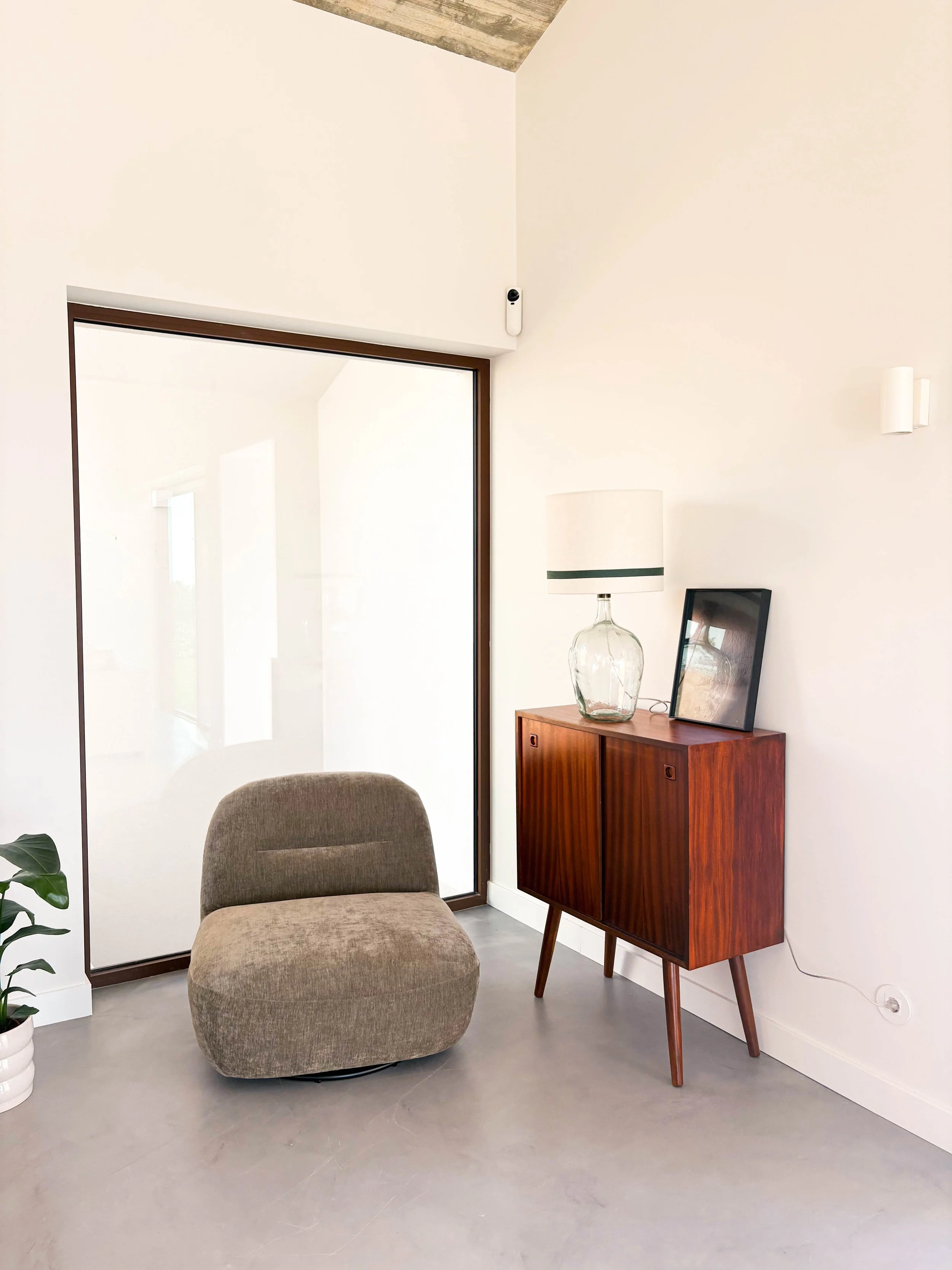 Sala de estar minimalista com uma poltrona bege, móvel de madeira e luminária em uma parede branca