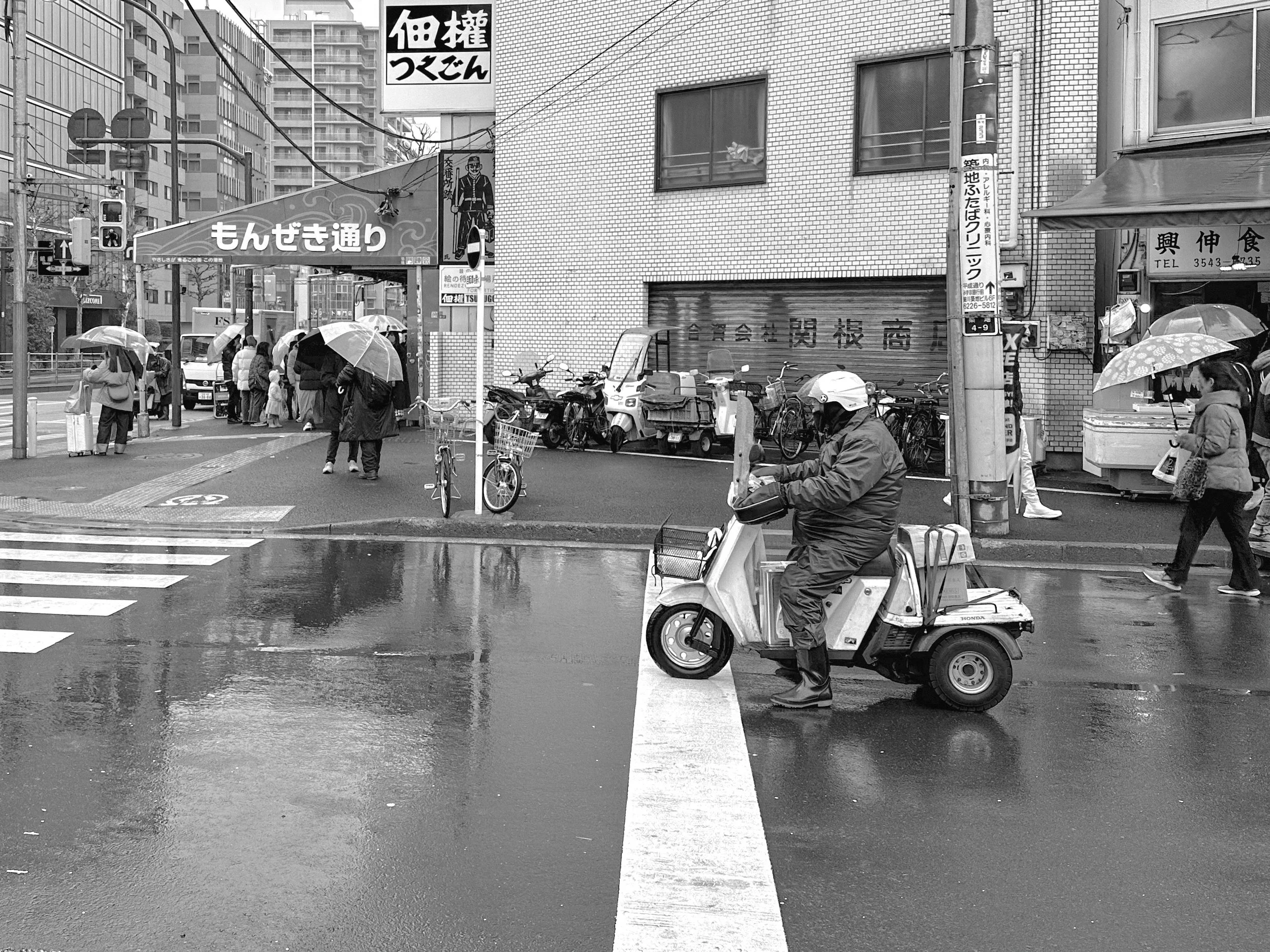 Delivery worker on a three-wheeled Honda moped in the rain at Tsukiji market, Tokyo, 2014. Black and white street photography by Aidan Martin
