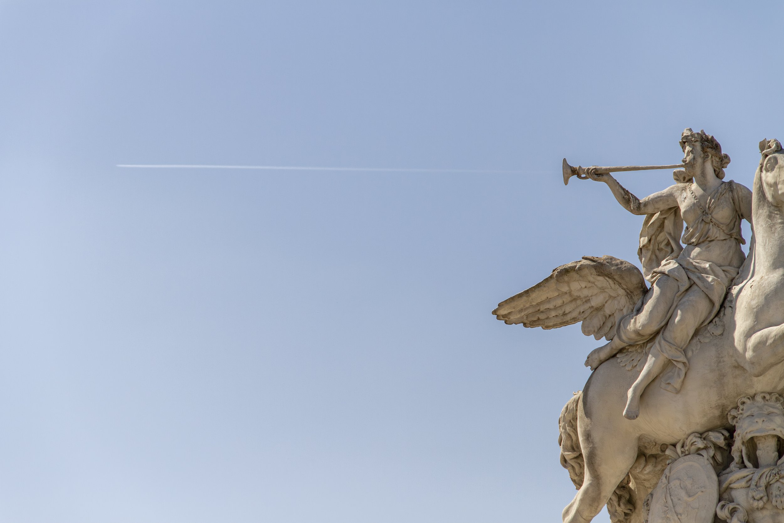 Winged bronze statue against a clear blue sky with a jet contrail crossing above, Paris, 2019. Fine art photography by Aidan Martin