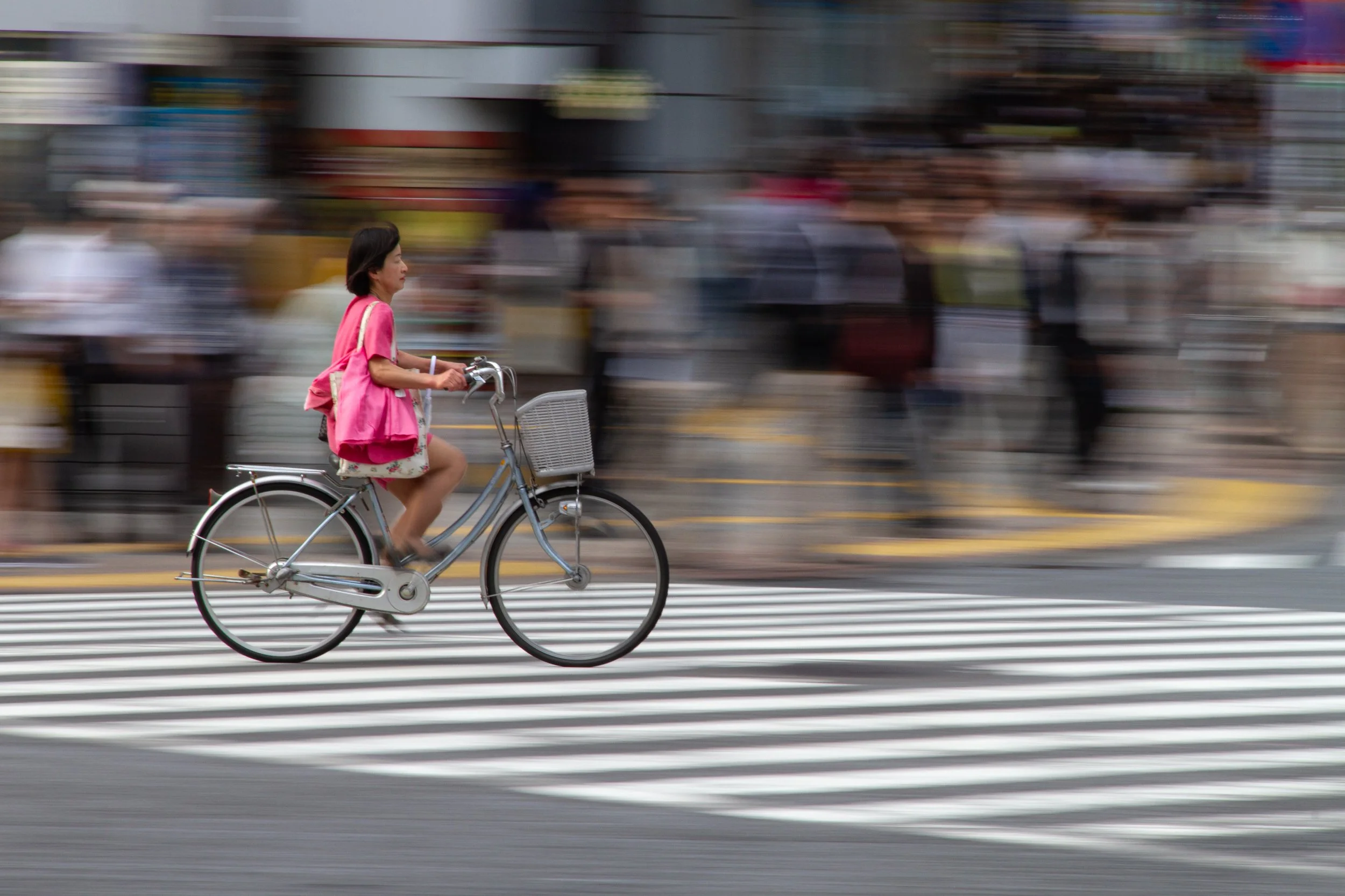 Woman in pink cycling across the Shibuya scramble crosswalk, Tokyo, motion blur panning shot, 2024. Street photography by Aidan Martin