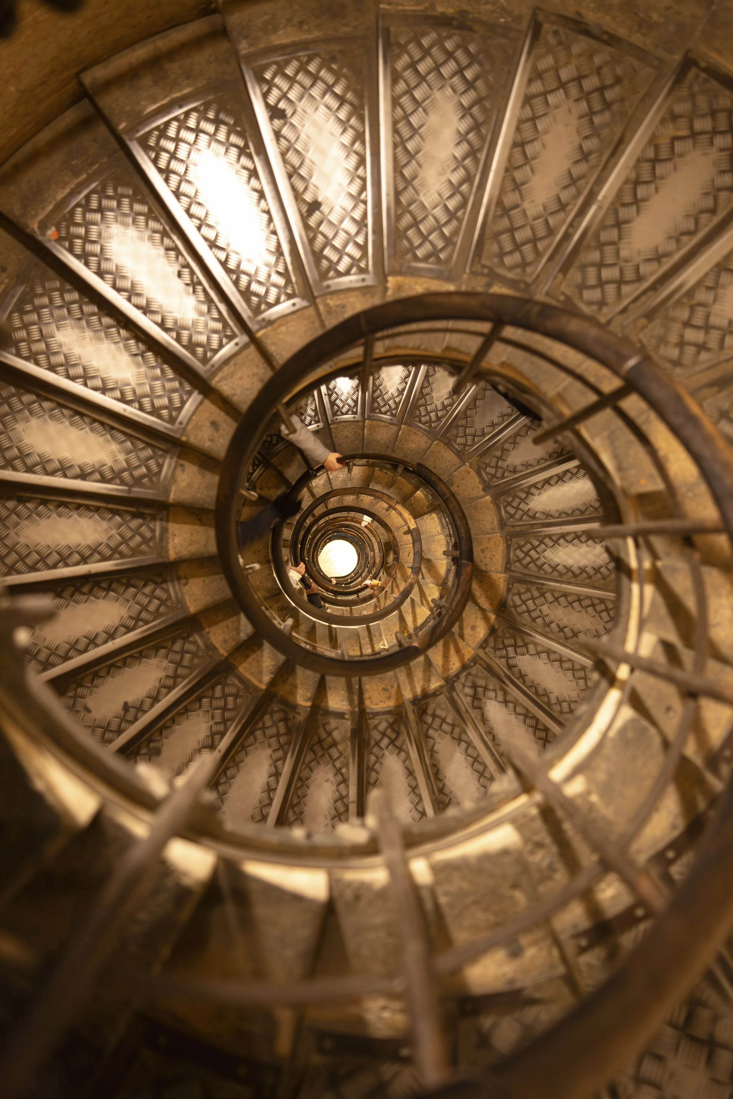Looking down the amber-lit spiral staircase inside the Arc de Triomphe, Paris, 2019. Architectural photography by Aidan Martin