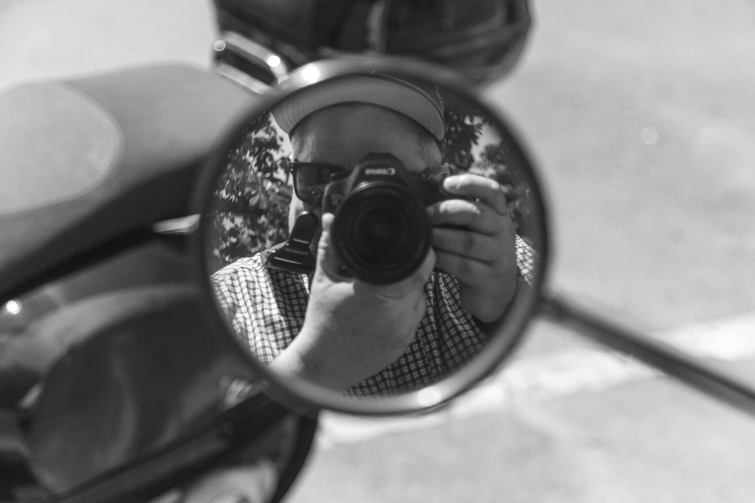 Photographer Aidan Martin reflected in a circular mirror while shooting, trees and sky behind. Black and white photography