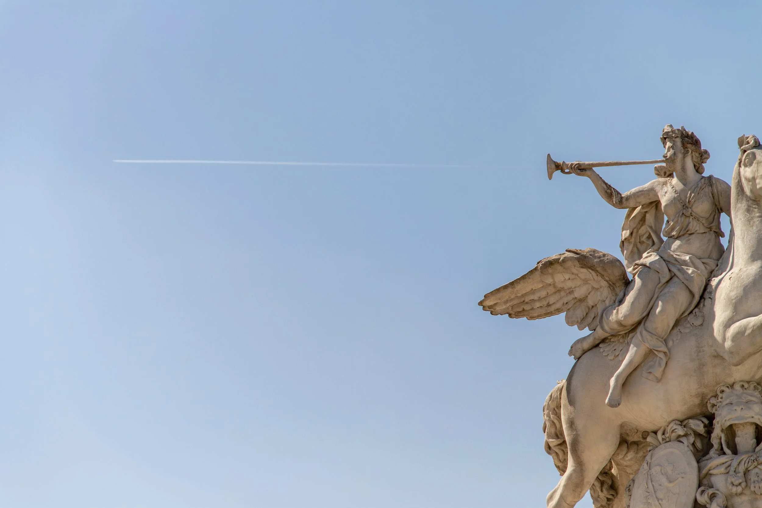 Winged bronze statue against a clear blue sky with a jet contrail crossing above, Paris, 2019. Fine art photography by Aidan Martin