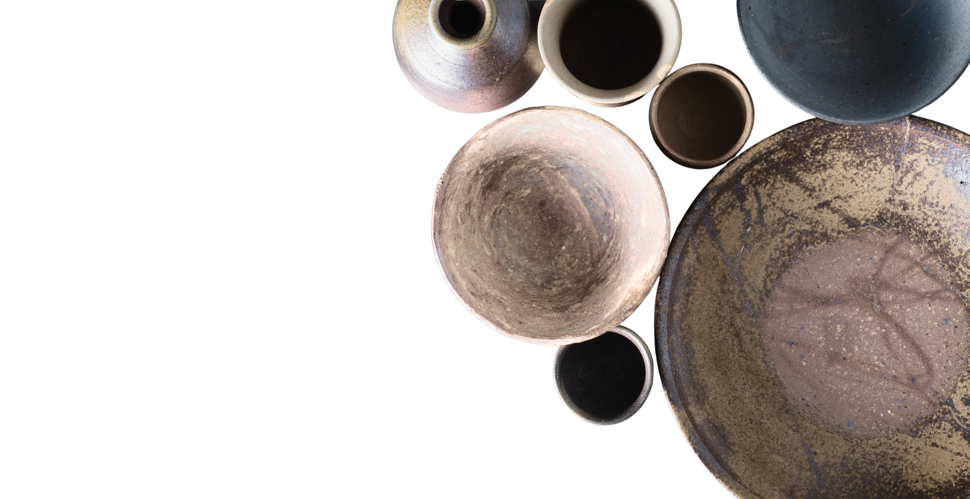 Top-down view of various rustic, textured ceramic and clay bowls and cups in natural earth tones, arranged on a black background.