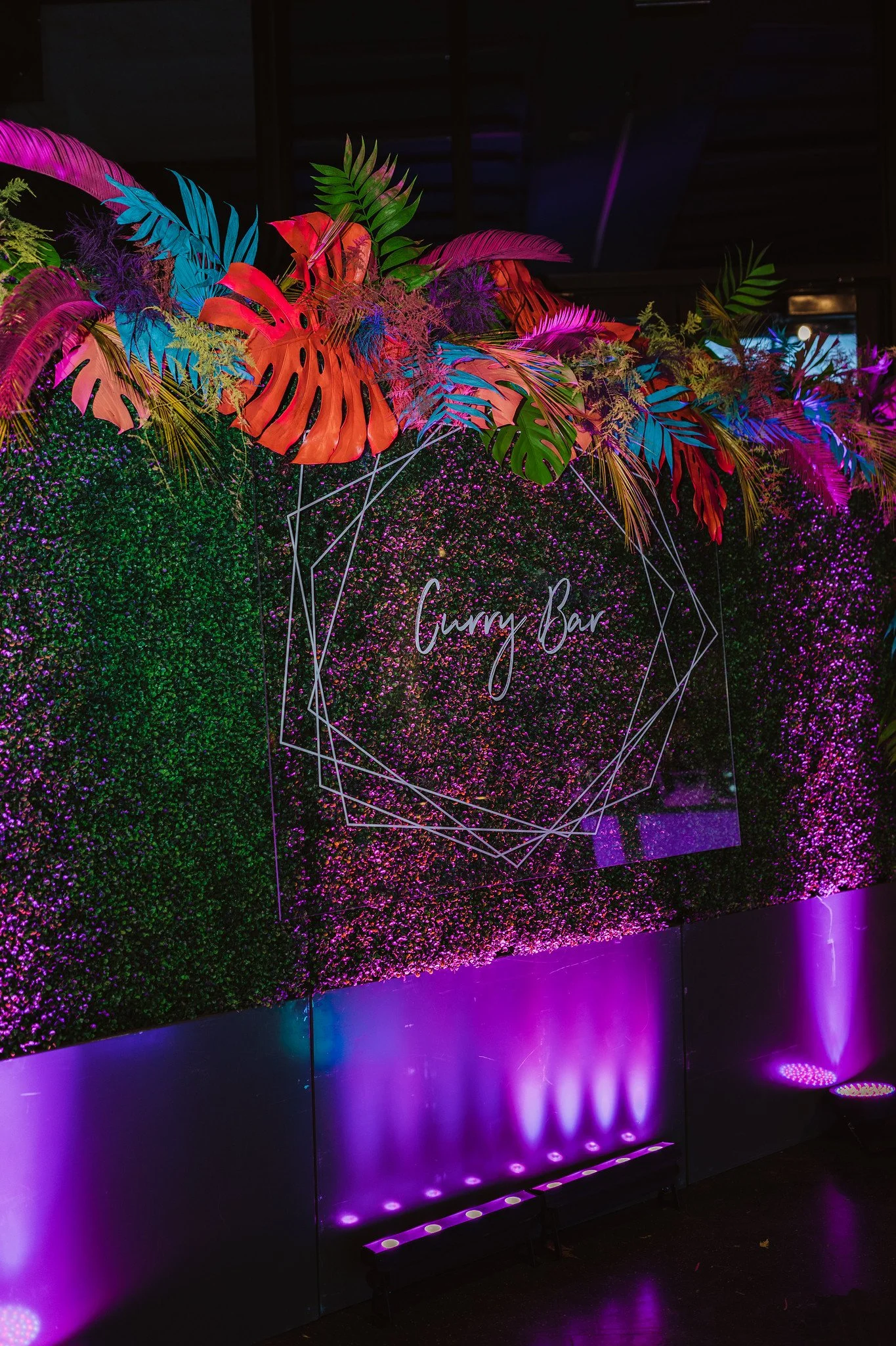 Neon sign reading 'Gummy Bar' surrounded by colorful tropical leaves and illuminated with purple and pink lights.