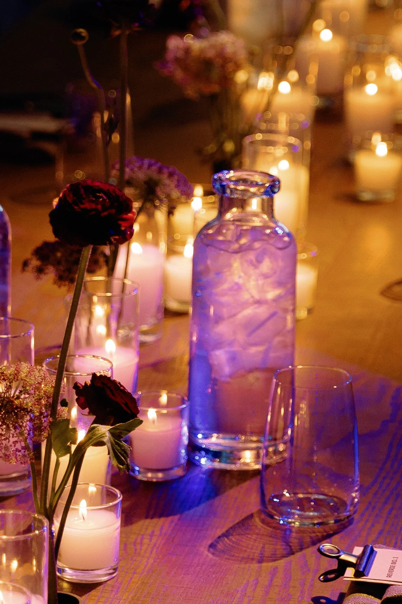 A dimly lit table with several candles, glass bottles, and flowers, creating a cozy, intimate atmosphere.