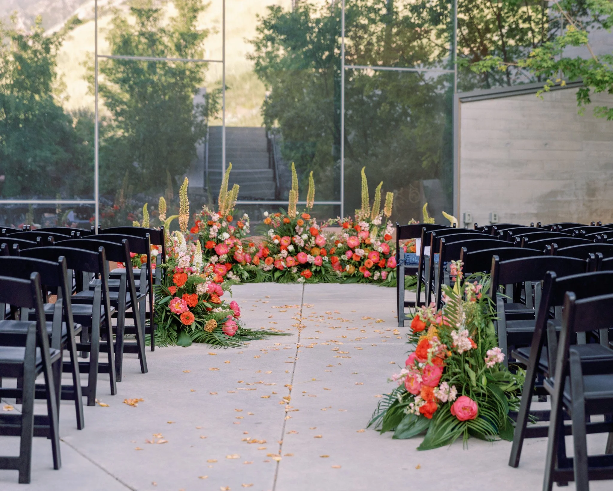Elegant event space decorated with round tables draped in beige and burnt orange tablecloths, adorned with floral centerpieces, and clear acrylic chairs.