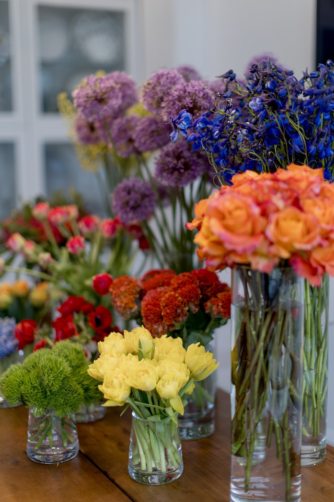 Various colorful flowers in glass vases on a wooden table, with a blurred background.