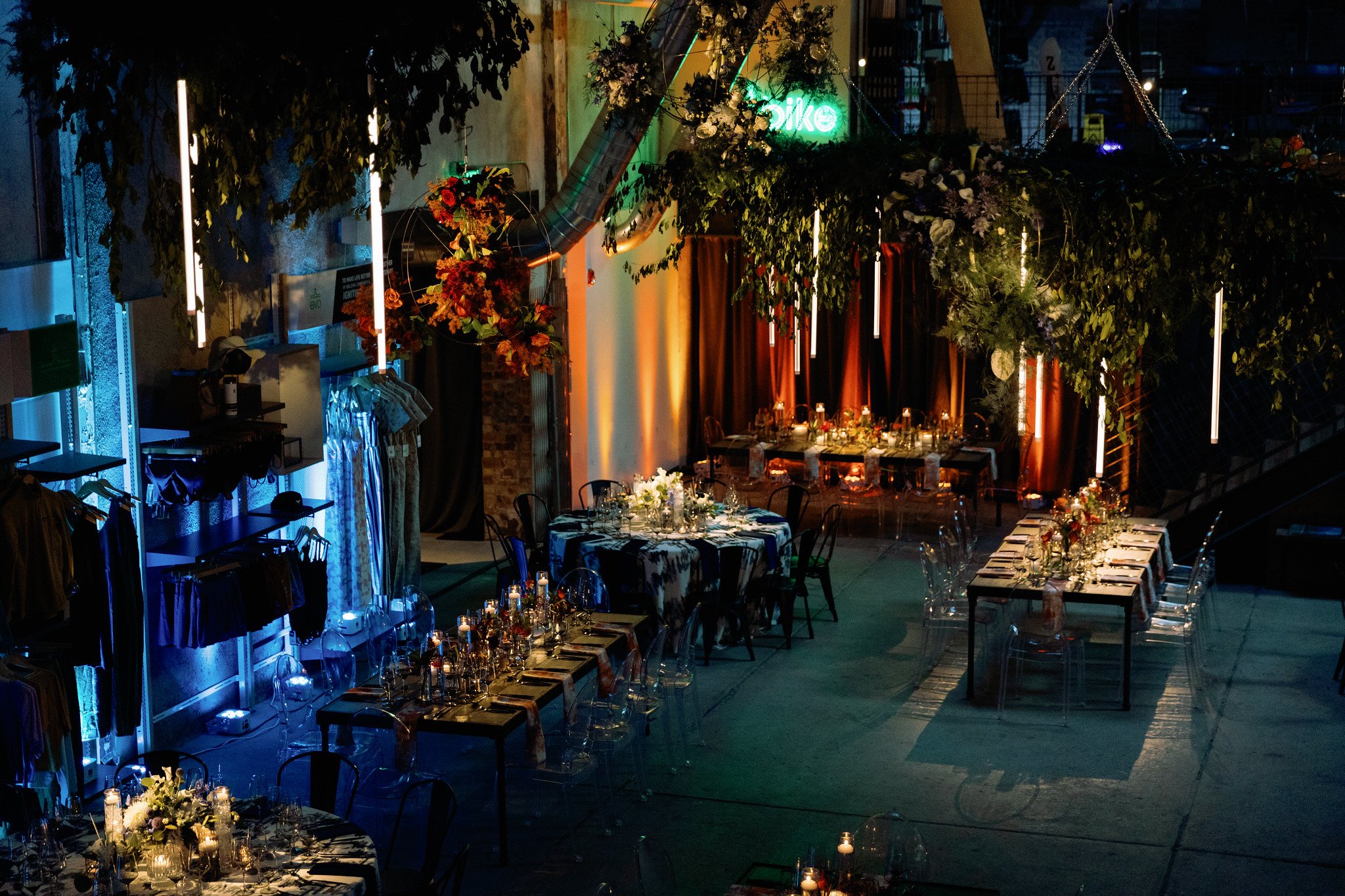 Indoor event space decorated with hanging plants, string lights, and tables set for dining, with a neon sign that says 'like' in the background.