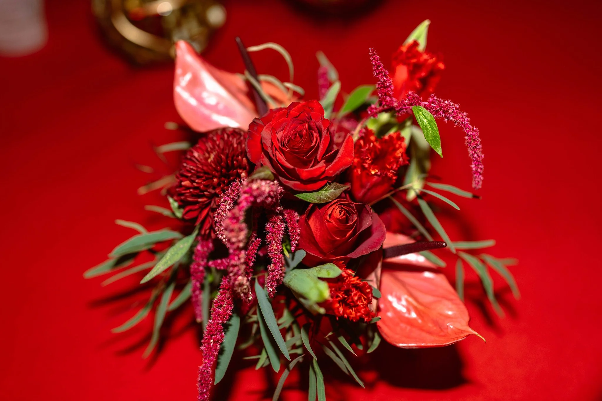 A bouquet of red roses, pink anthuriums, and various red and pink flowers with green leaves on a red background.