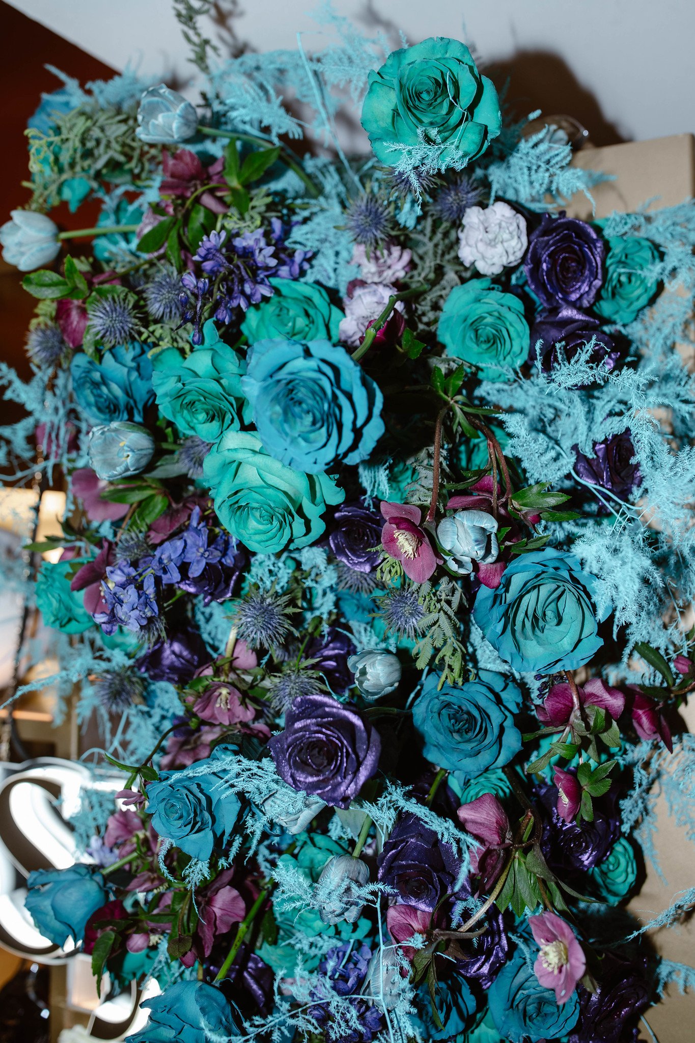 Arrangement of various blue, purple, and white flowers with greenery and textured foliage.