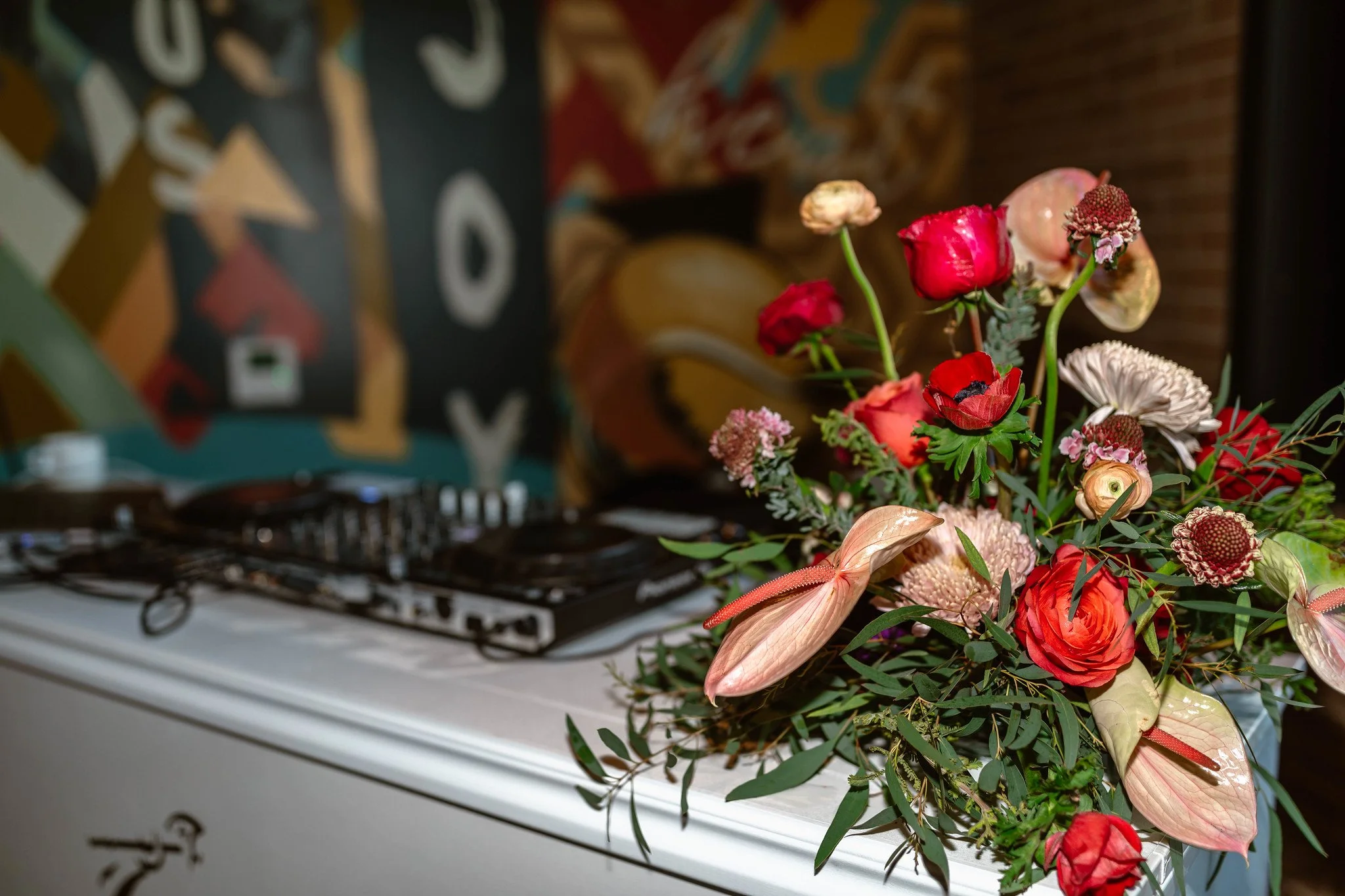 A floral arrangement with red, pink, and peach flowers resting on a DJ keyboard at a party or event.