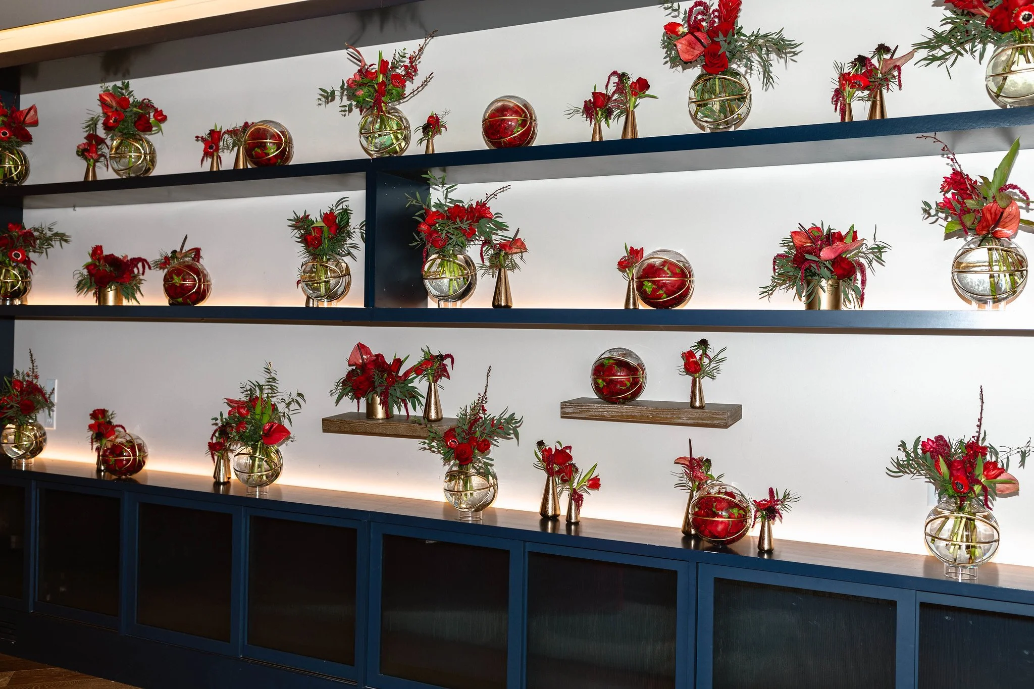 Display shelves with red floral arrangements and gold and glass vases.