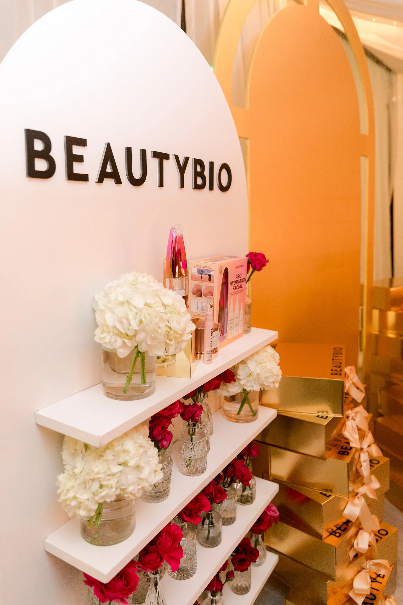 Display shelf holding clear glass vases with white and pink flowers, skincare products, and promotional materials at a beauty store.