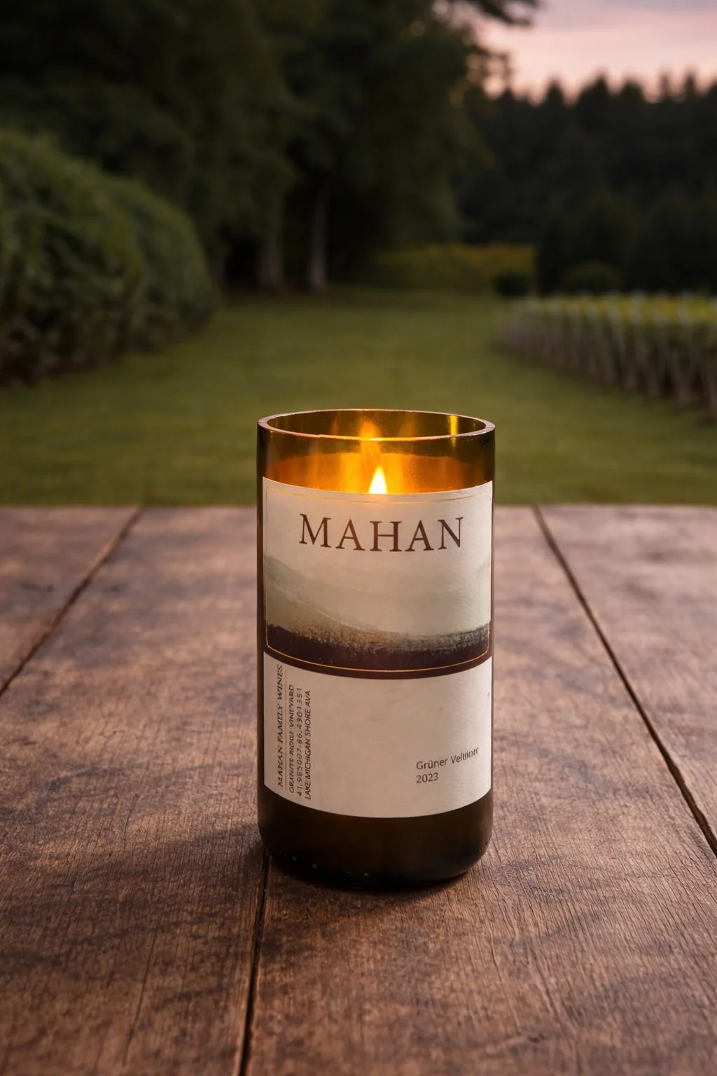 A lit candle made from repurposed wine bottle from Mahan Family Wines.  It sits on a wooden table outdoors at Granite Ridge Vineyard at sunset.
