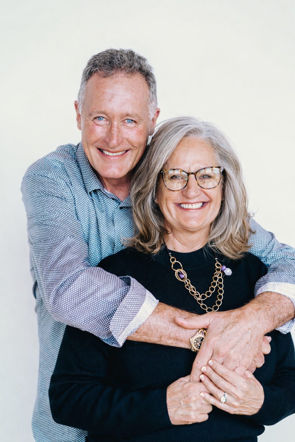 An older couple smiling and embracing each other against a plain white background.