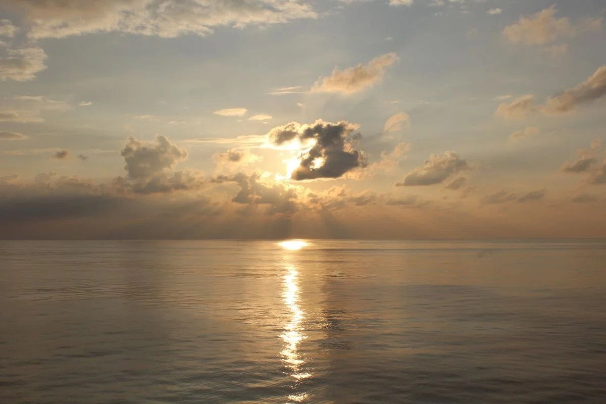 Sunset over a calm ocean with scattered clouds in the sky.