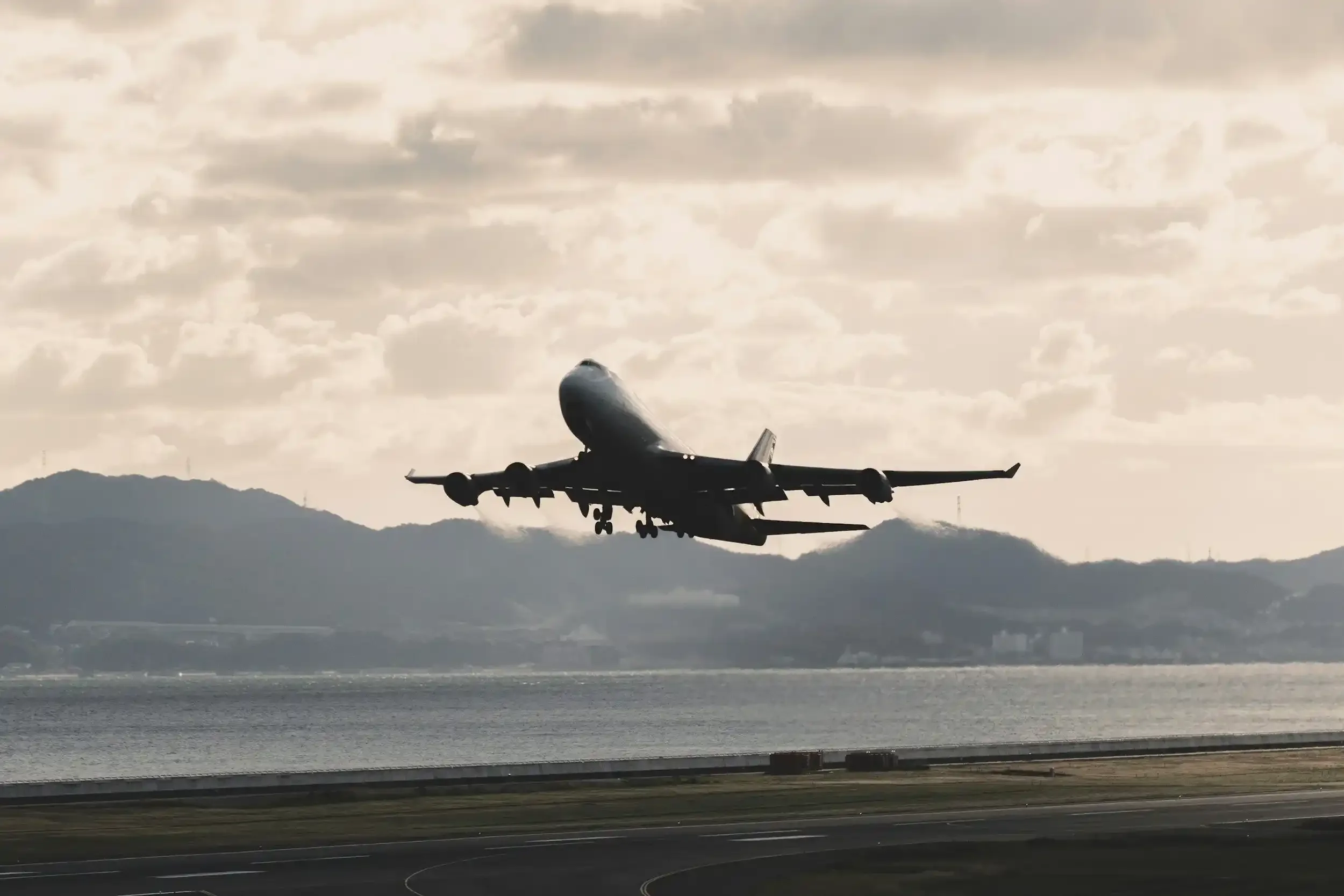 An airplane taking off or landing on a runway, with mountains and a cloudy sky in the background.
