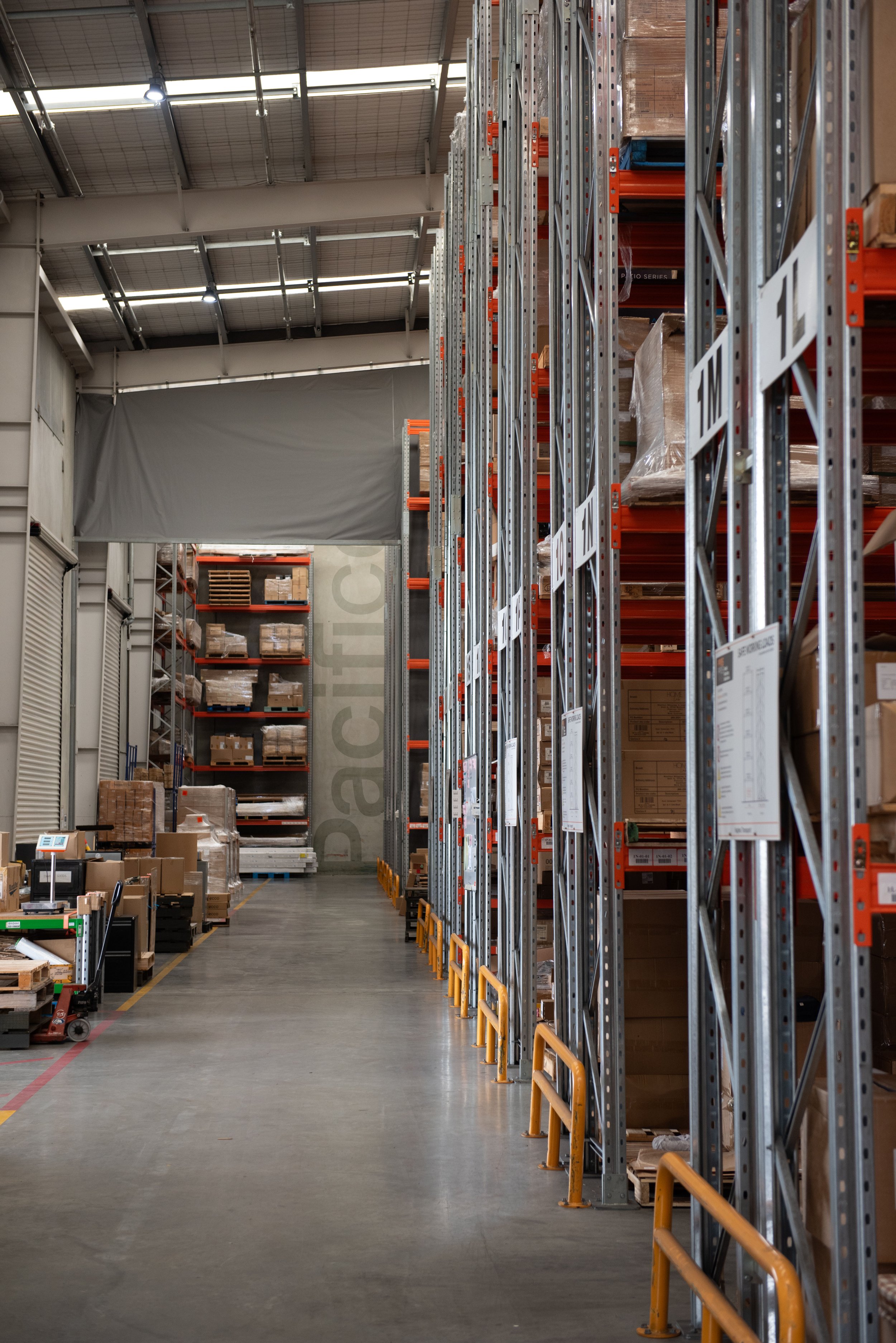 Interior of a warehouse with metal shelves stocked with boxes and pallets, and a wide aisle for storage and movement.