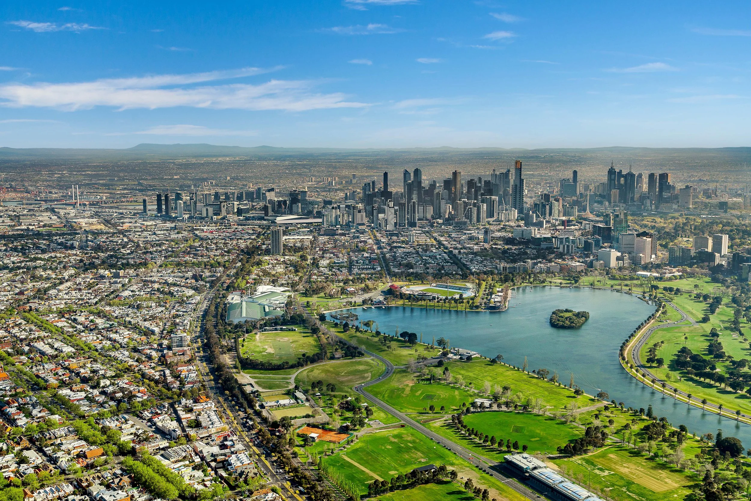 Aerial view of a city with tall skyscrapers, a large park with a lake, and surrounding neighborhoods on a sunny day.