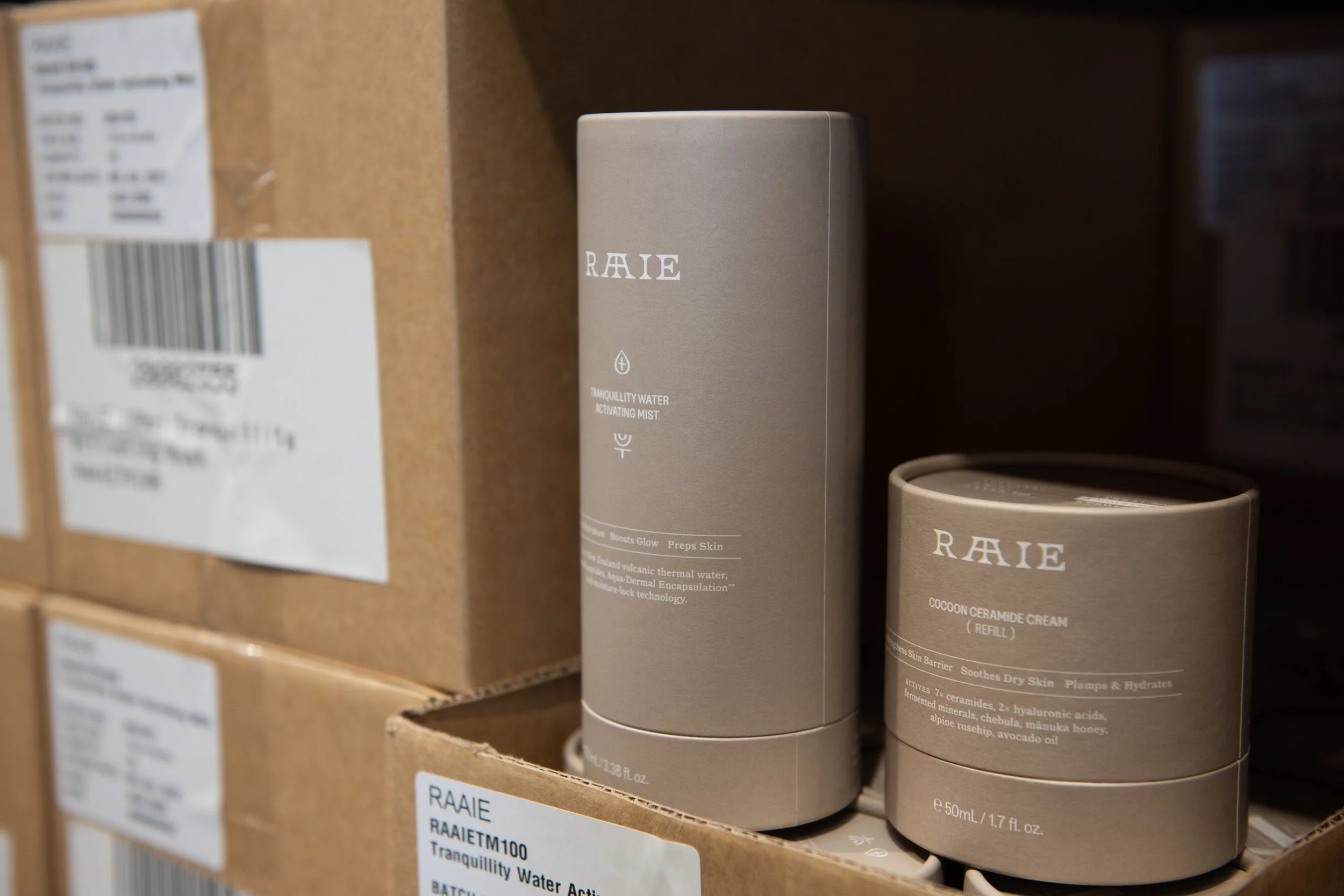 Close-up of skincare product containers on a store shelf, including a beige cylindrical bottle labeled "RAIE" and "Cocoon Ceramide Cream Refill" with additional descriptive text.