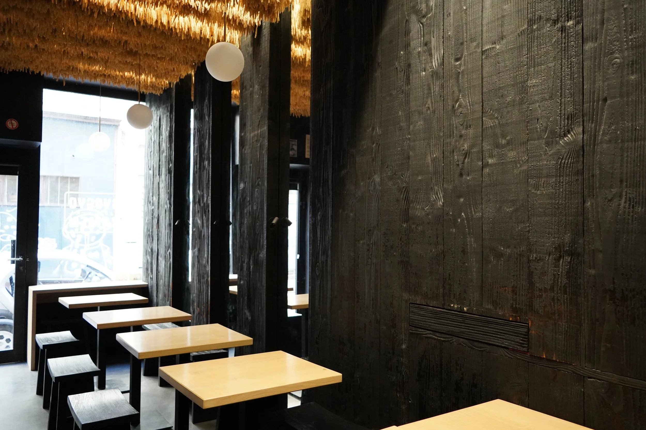 Intérieur d'un restaurant avec murs en bois foncé, plafond décoratif en éléments clairs, et tables en bois clair avec des bancs noirs.