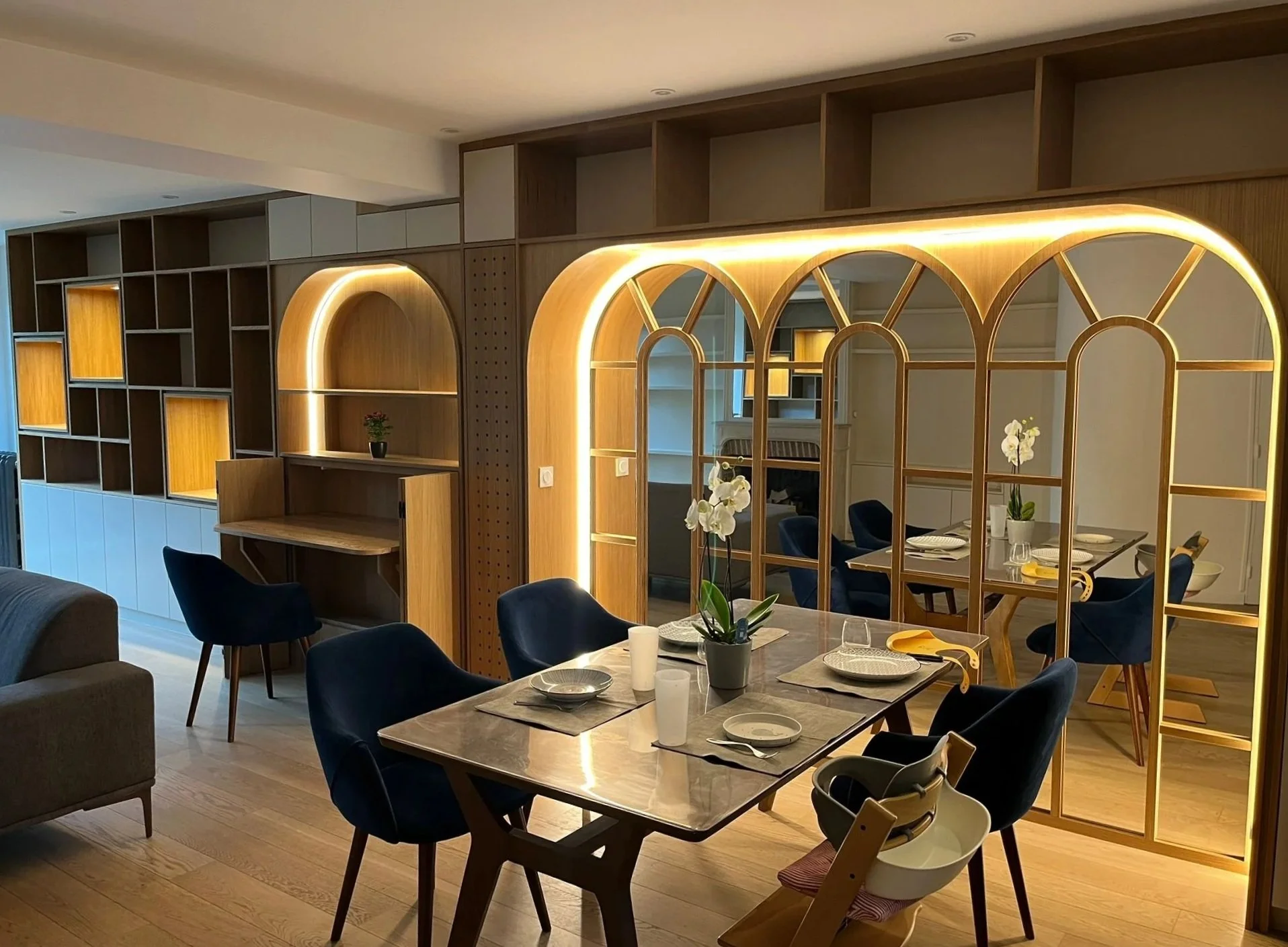 Intérieur moderne d'une salle à manger avec une table dressée, des chaises en bois et des étagères en bois avec éclairage LED intégré.