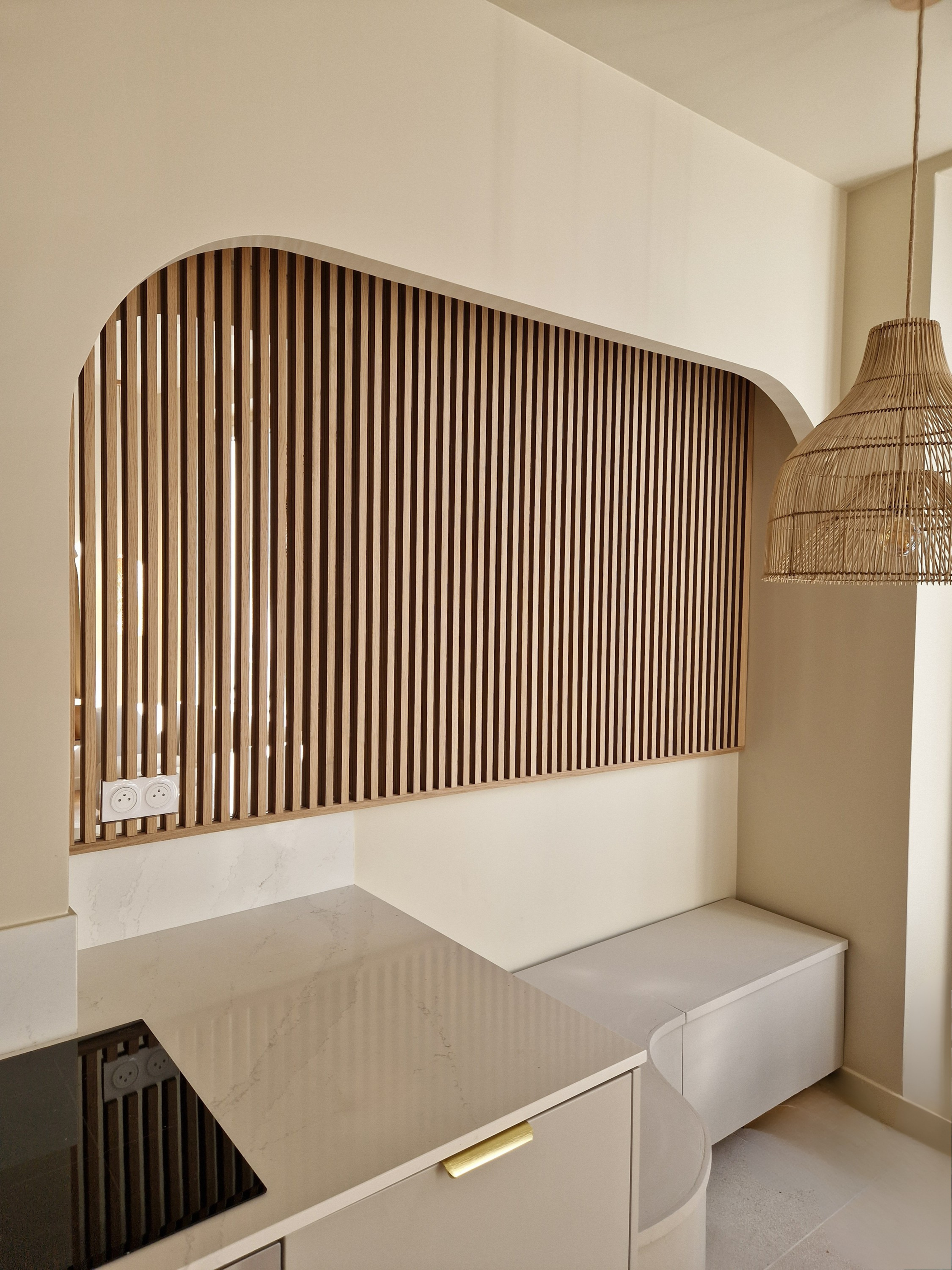 Vue intérieure d'un espace de travail moderne avec une cloison en bois, un comptoir en marbre beige, des prises électriques, et un lampe en rotin suspendue.