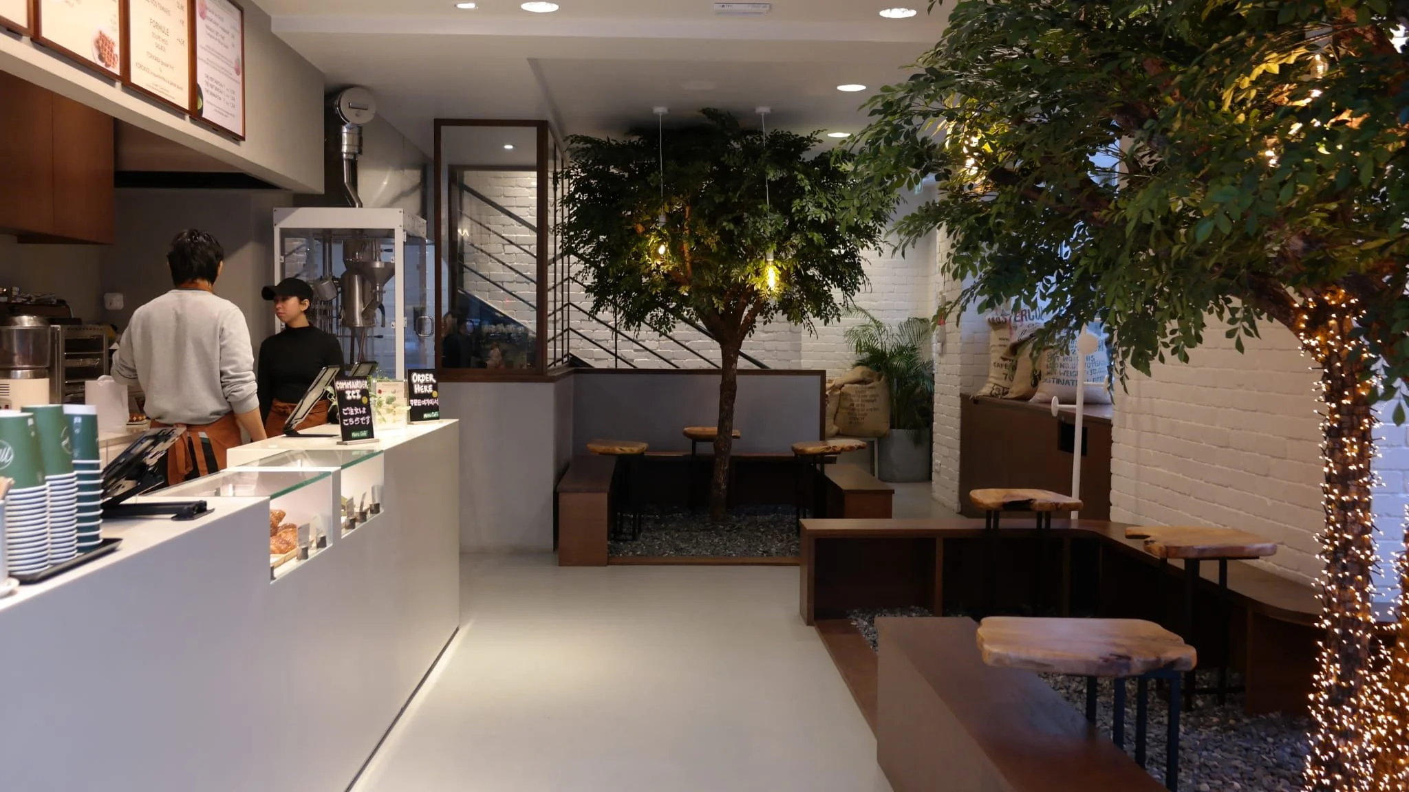 Intérieur d'un café avec un comptoir où deux employés discutent, décorée avec des arbres et des lumières