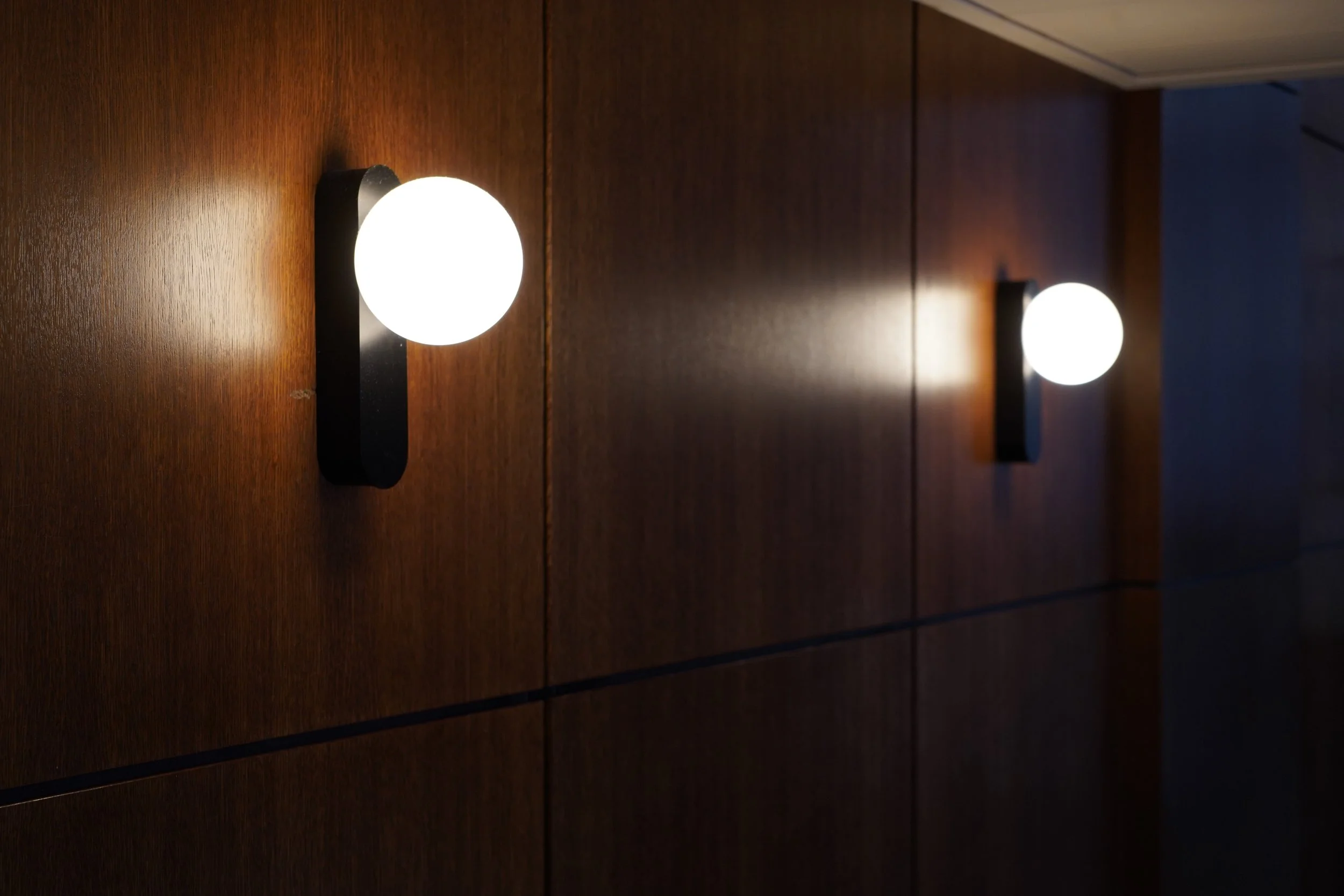 Deux luminaires ronds montés sur un mur en bois, éclairant une pièce sombre.